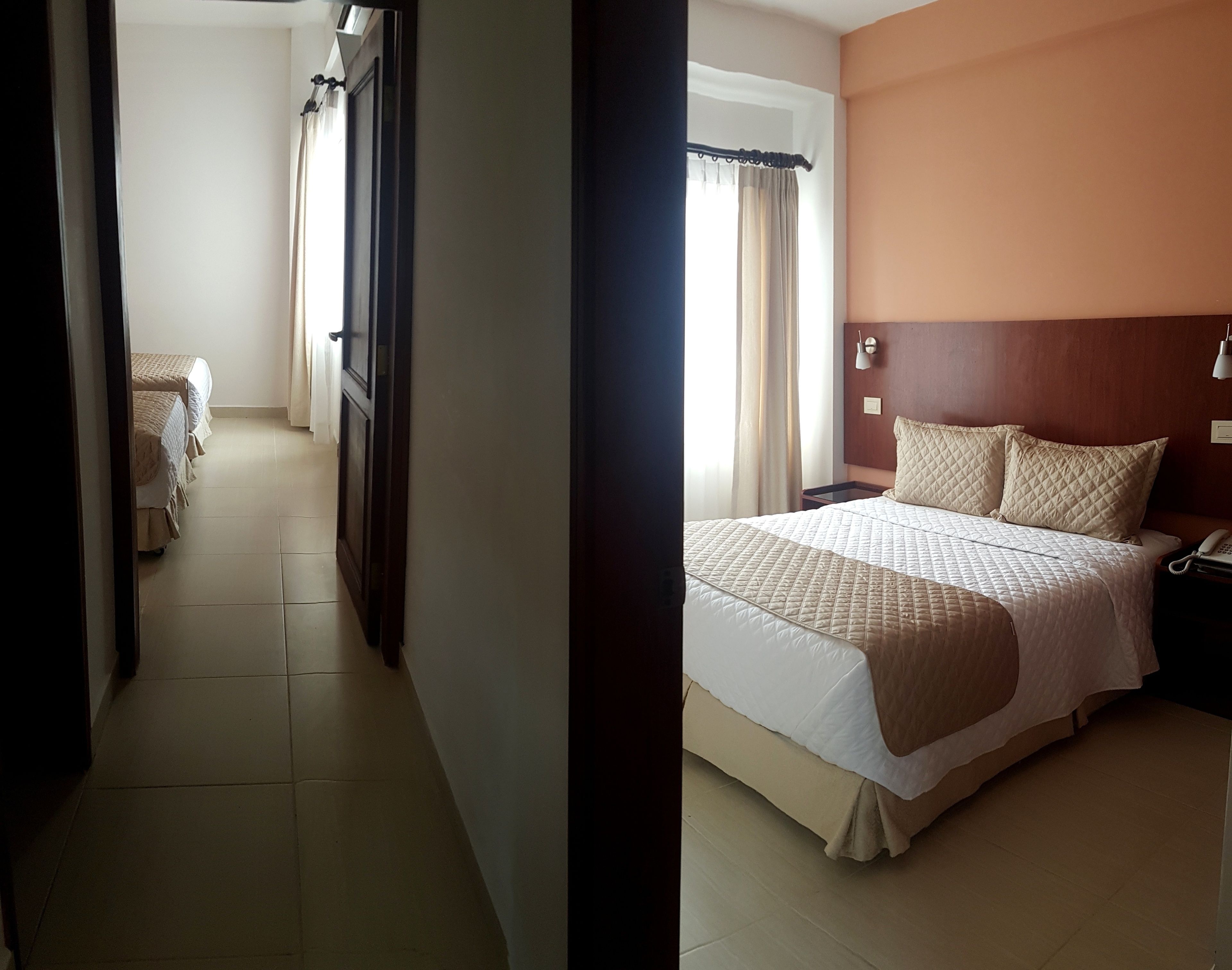 Une chambre d’hôtel avec un grand lit, une table de chevet avec une lampe et une vue sur le couloir.