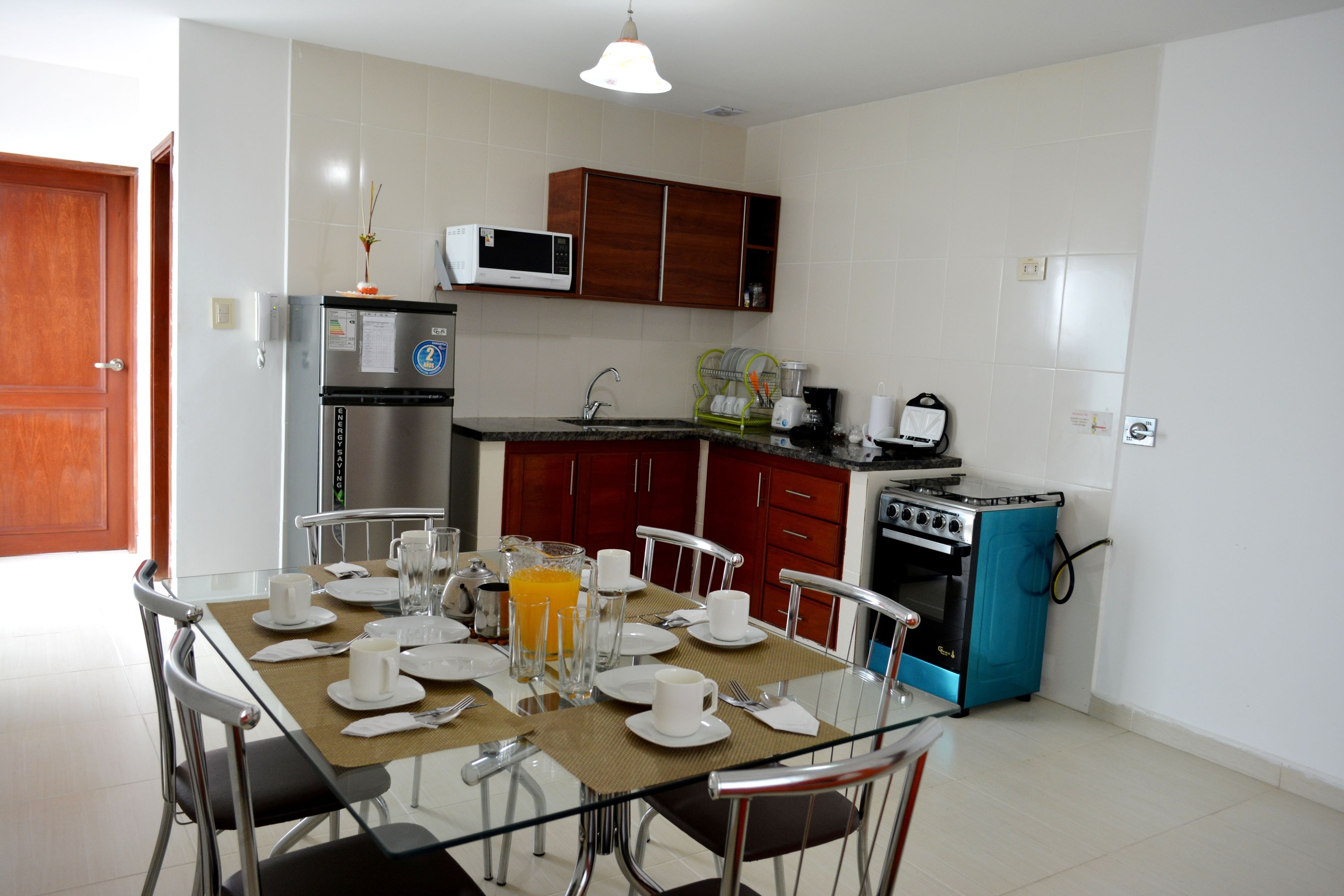 Une cuisine moderne avec une table à manger dressée pour le petit-déjeuner, comprenant des assiettes, des tasses et un verre de jus d’orange.