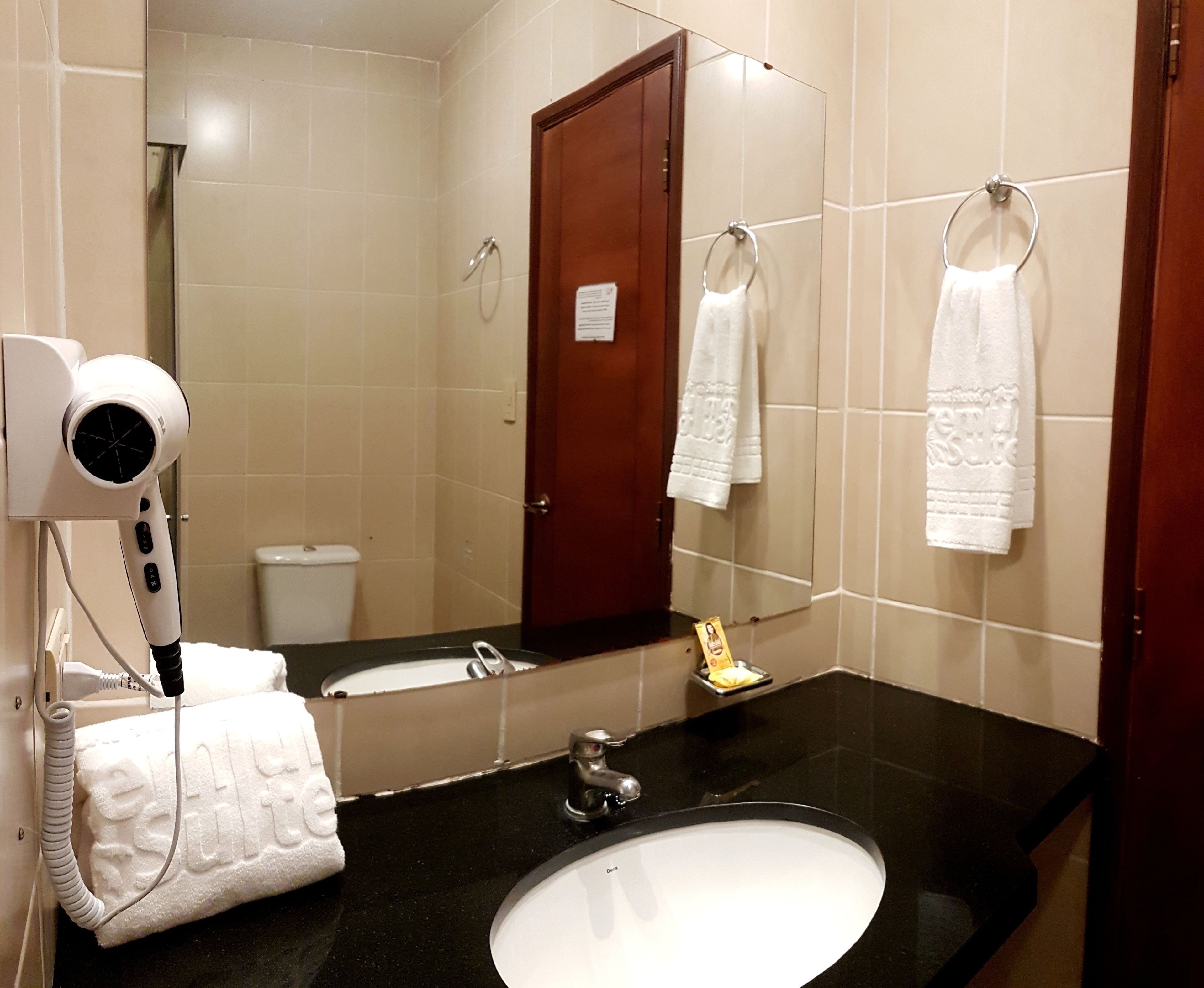 Un baño con encimera negra, lavabo blanco, espejo y secador de pelo.