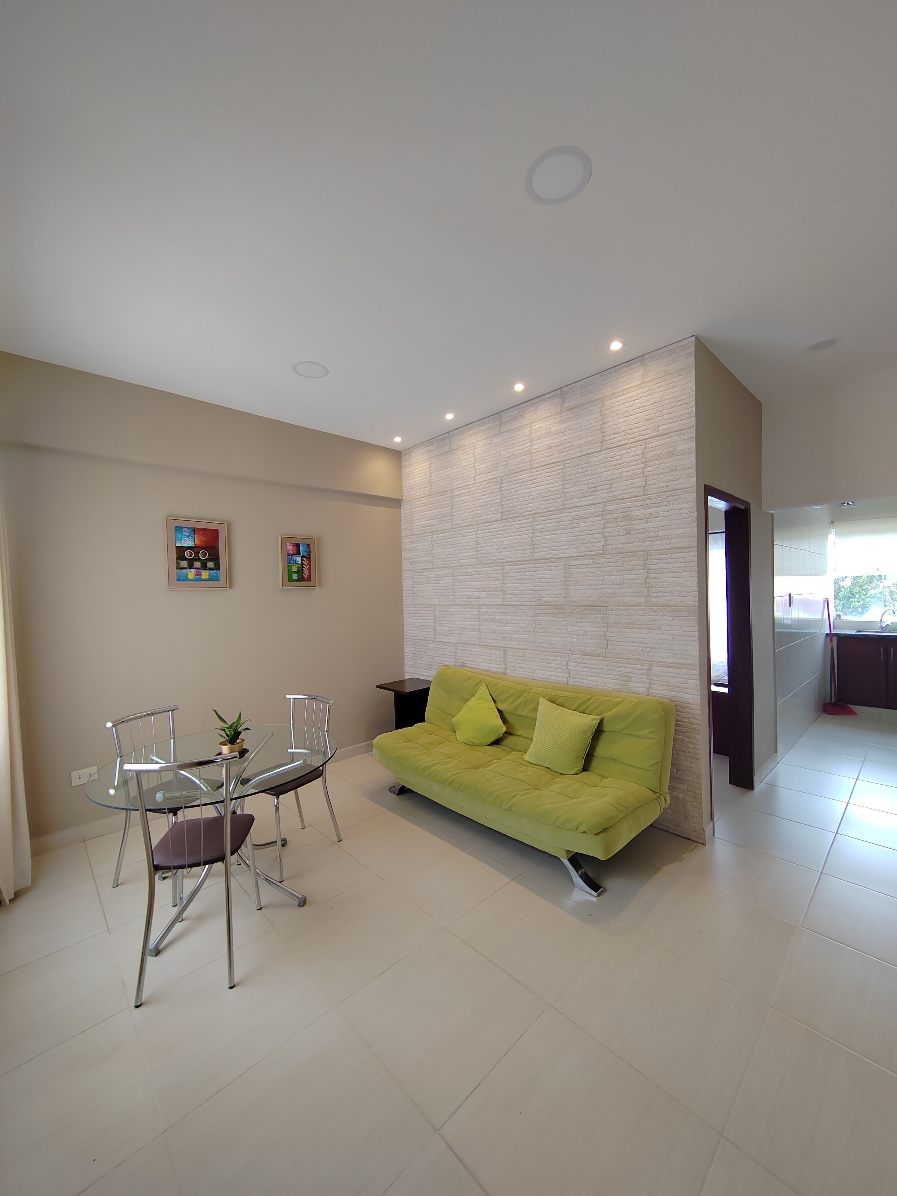 Una sala de estar moderna con una mesa de comedor de vidrio, un sofá verde y una pared de ladrillo blanco como detalle.