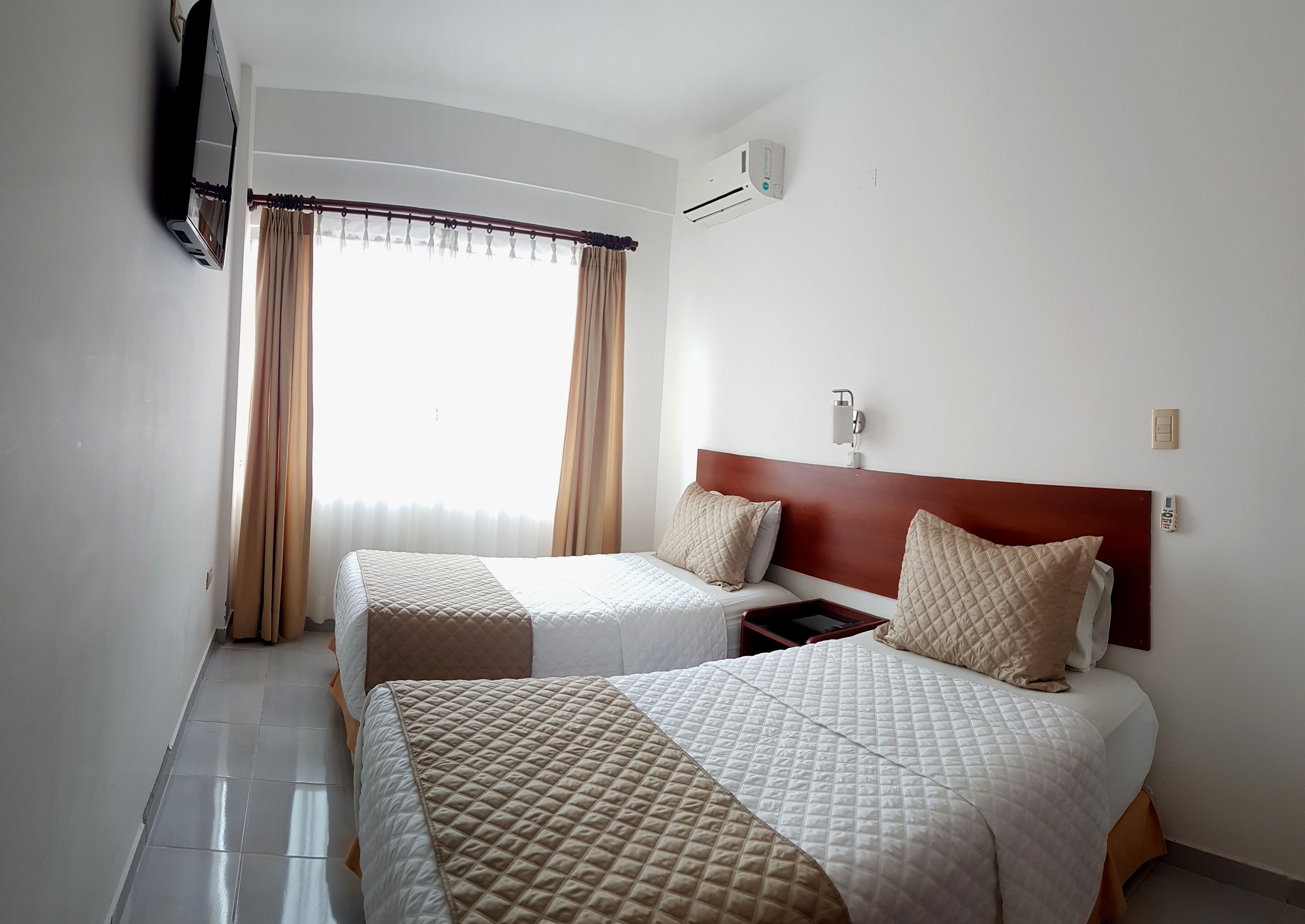 Quarto de hotel com duas camas, uma televisão, ar condicionado e uma mesa de cabeceira com telefone.