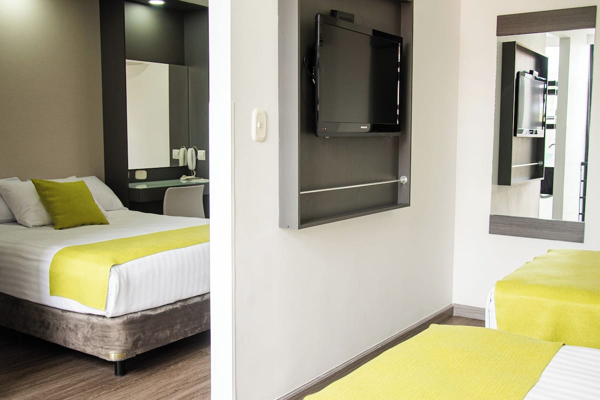A hotel room with two beds, a desk, a mirror, and a television.
