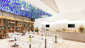 A modern restaurant with white furniture, a colorful ceiling, and a kitchen area with a TV.