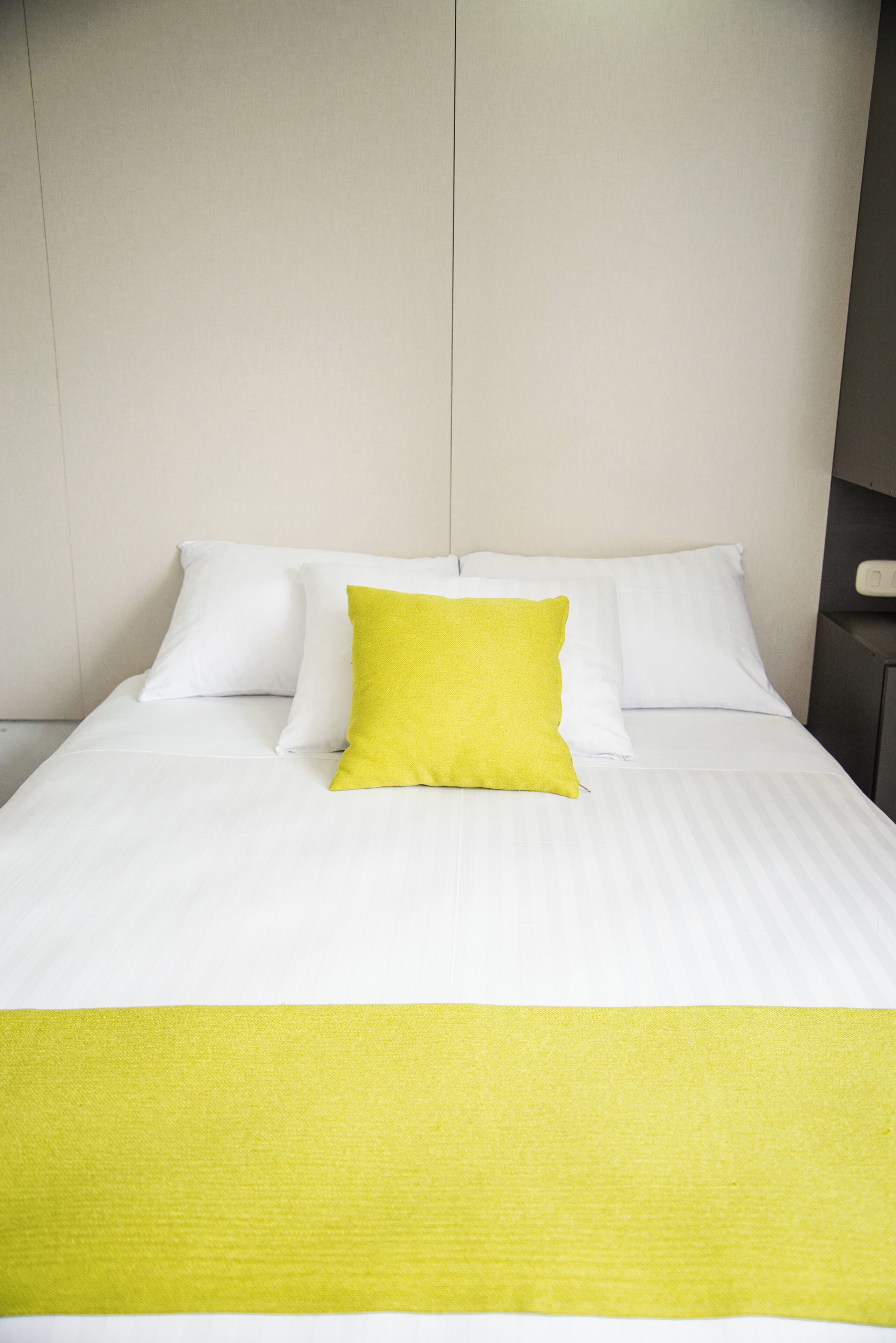 A neatly made bed with white linens and a single bright yellow pillow.