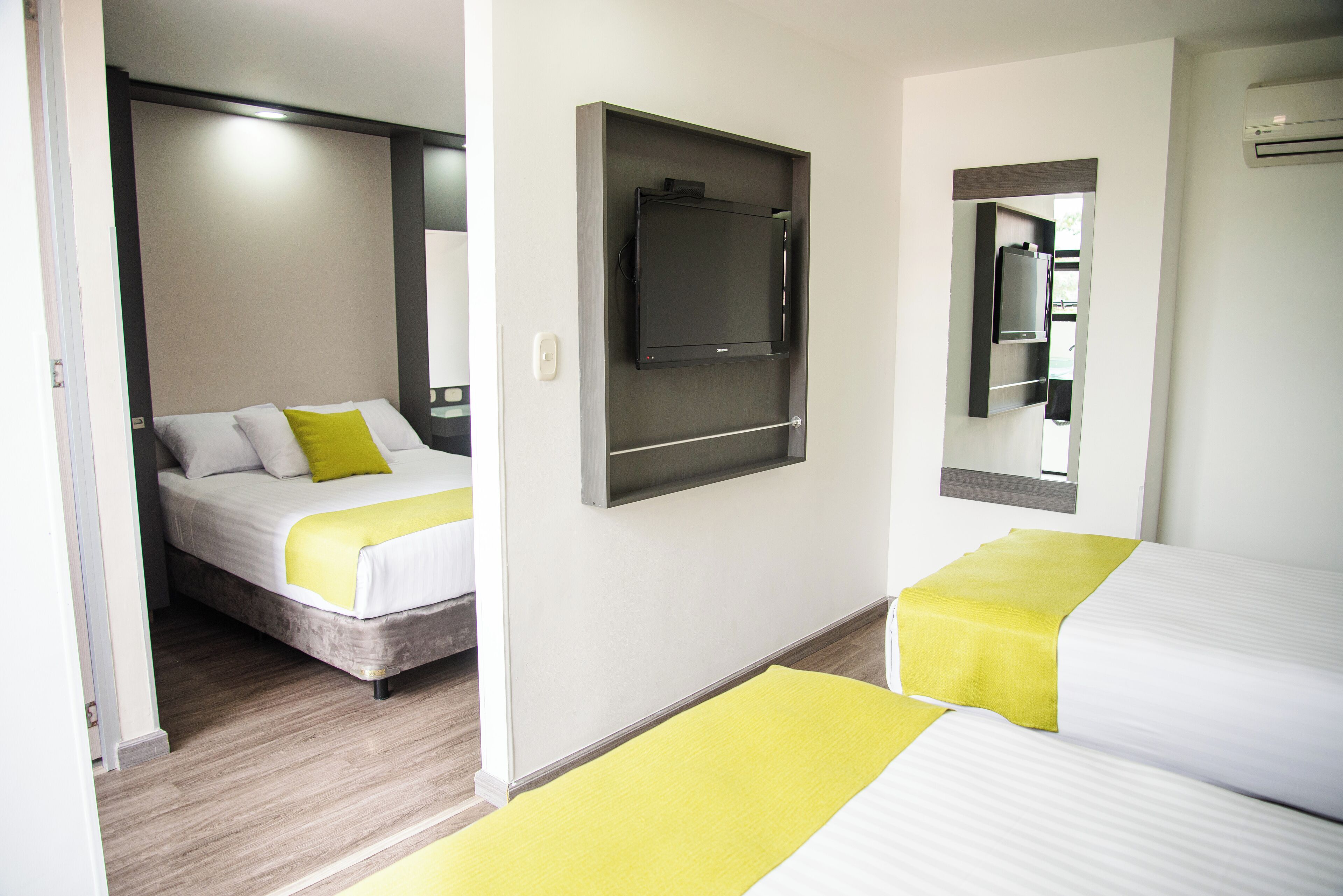 A hotel room with two beds, a flat-screen TV mounted on the wall, and a mirror above the bed.