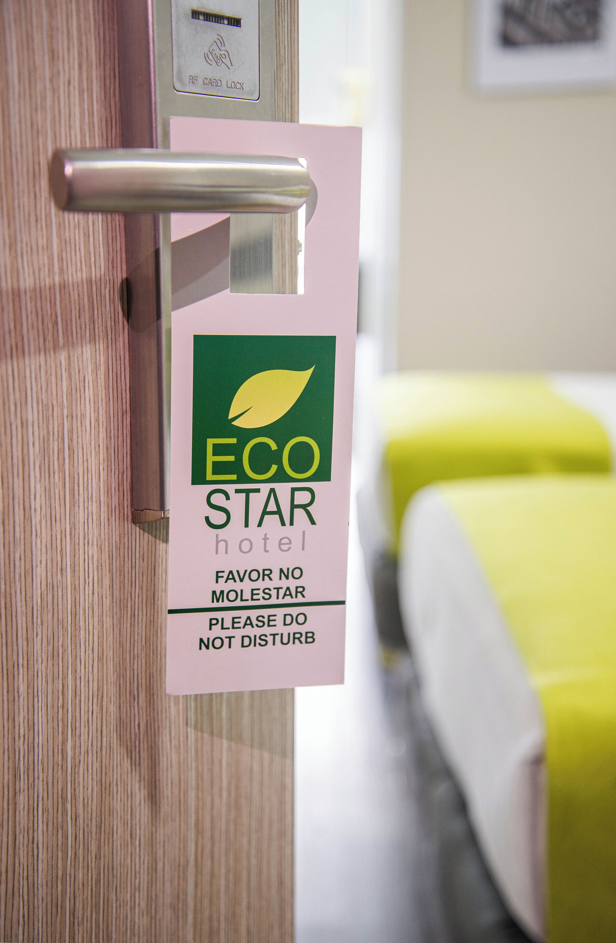 A door with a sign for the ECO STAR hotel, a keycard reader, and a bed with a yellow cover.