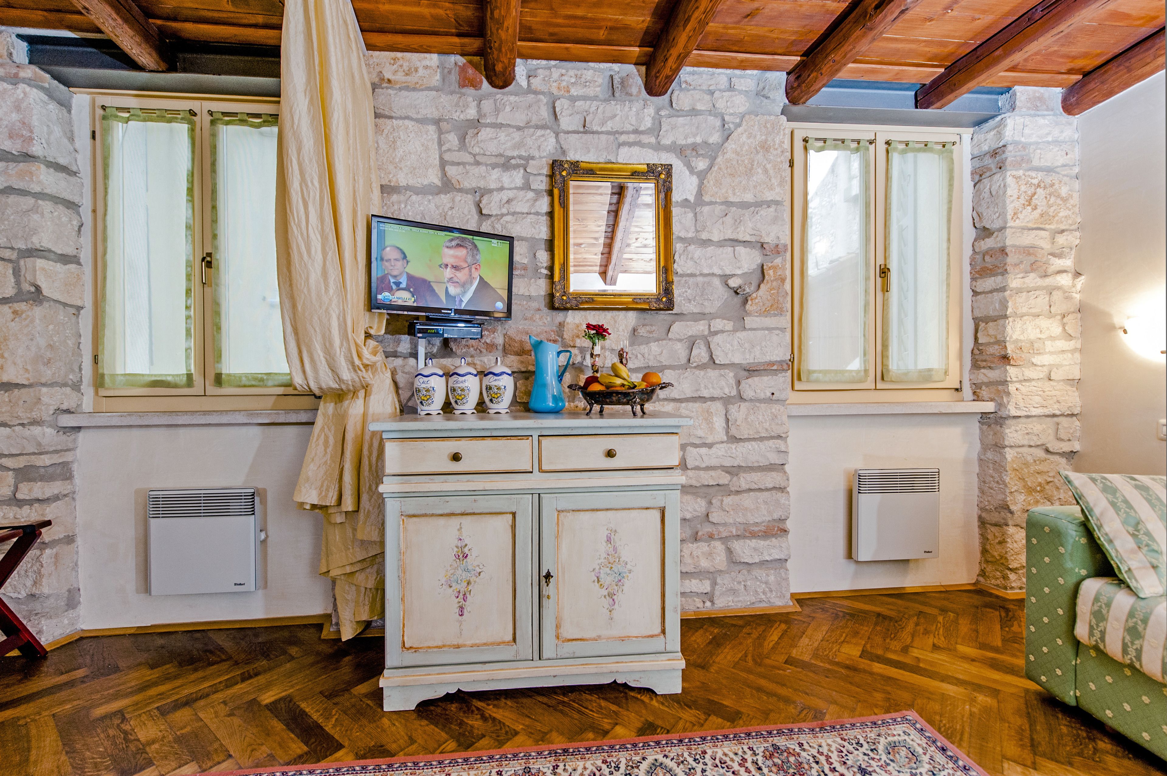 A cozy room with stone walls, wooden beams, a vintage cabinet, a television, and a green sofa.