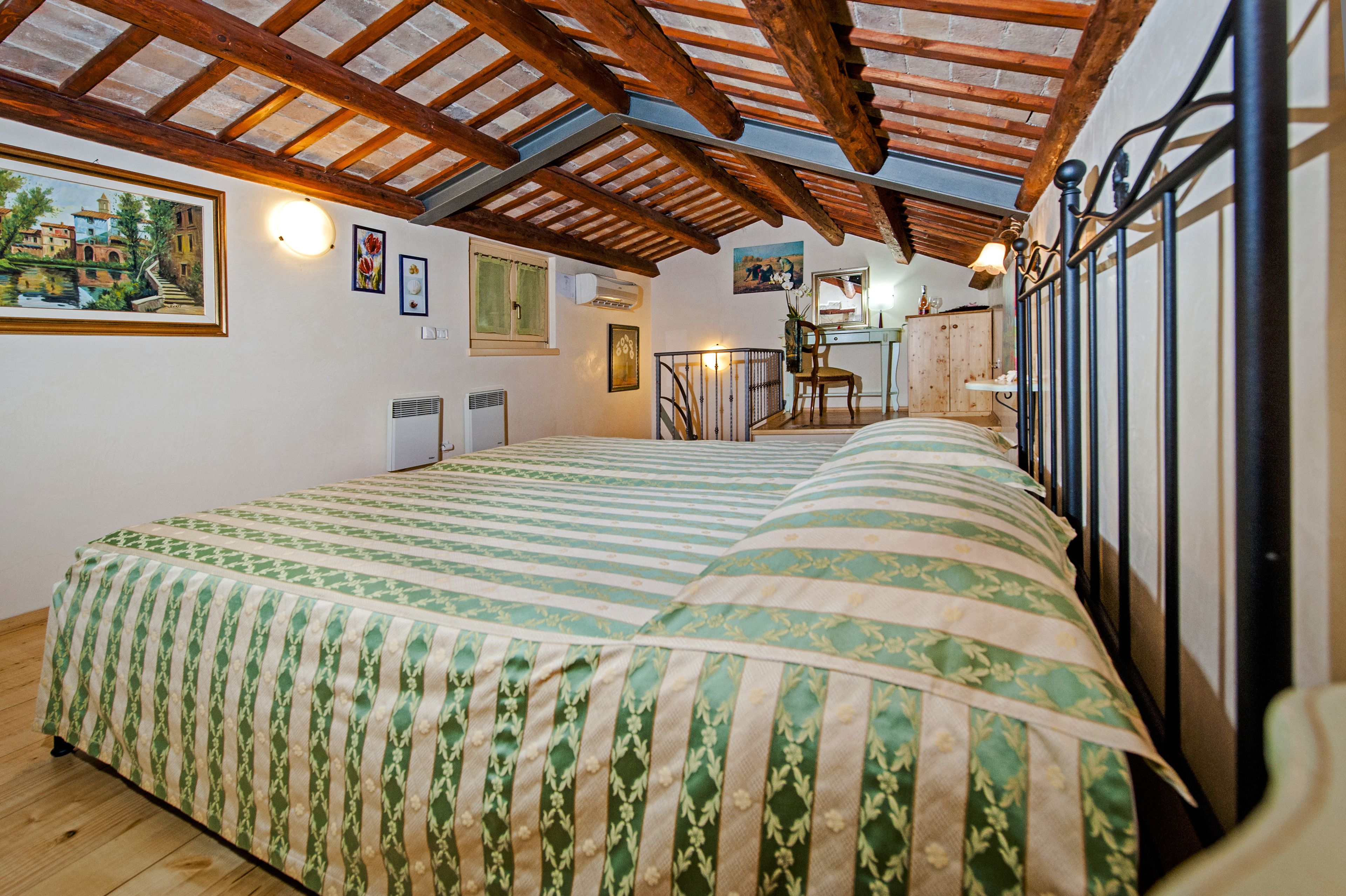 Un dormitorio con una cama grande, vigas de madera en el techo, un escritorio y una silla.
