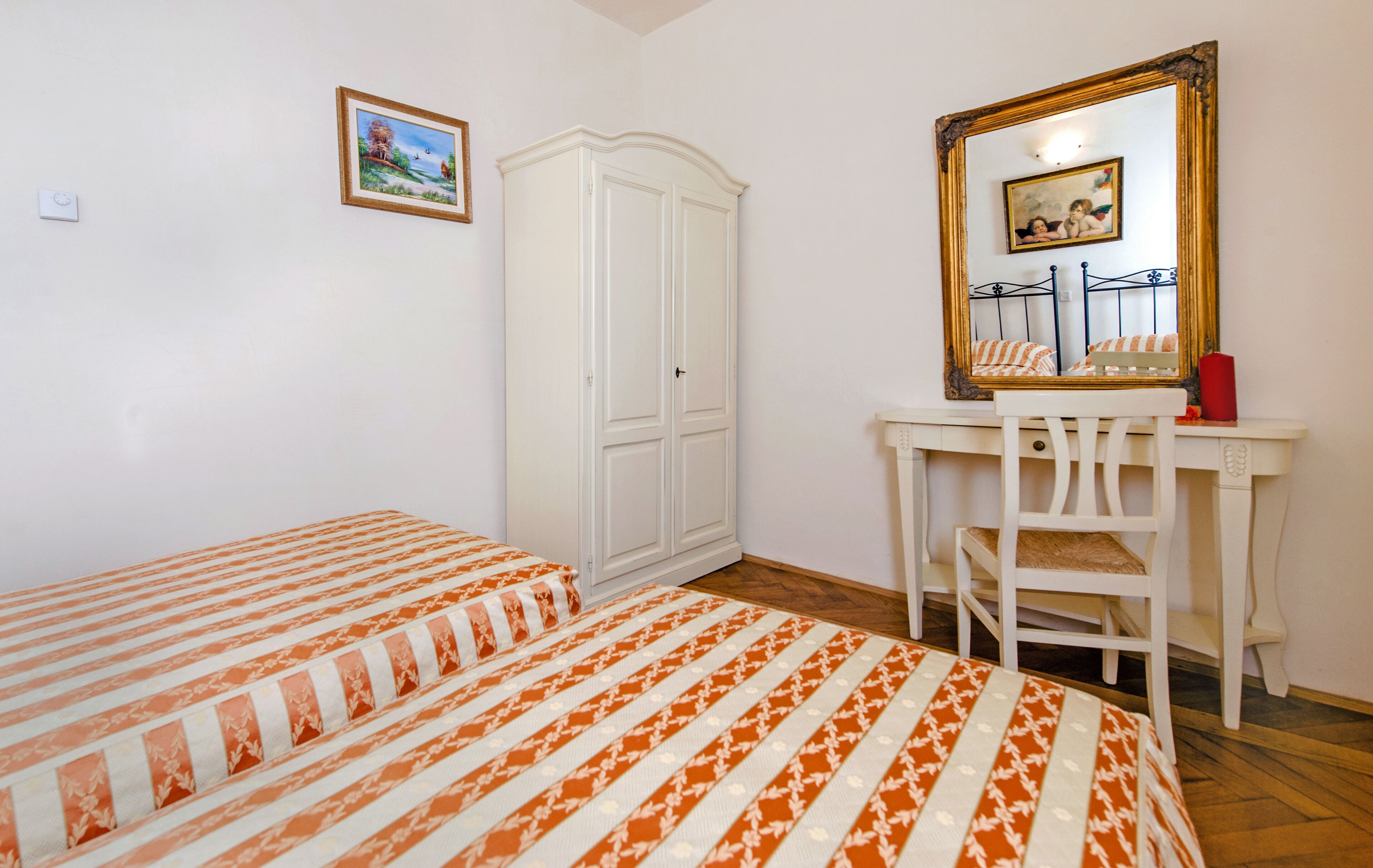 A bedroom with two beds, a wardrobe, a desk with a chair, and a mirror.