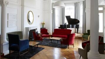 Un salón amplio con un piano de cola, sillones rojos y azules, y una chimenea.