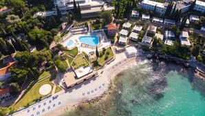 An aerial view of a coastal resort with a swimming pool, beach, and multiple hotel buildings.