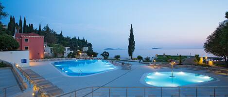A swimming pool area with multiple pools, a staircase, and a view of the sea.
