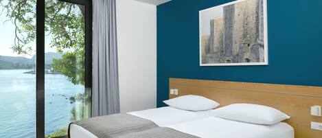 A hotel room with a bed, a view of a body of water, and a painting on the wall.