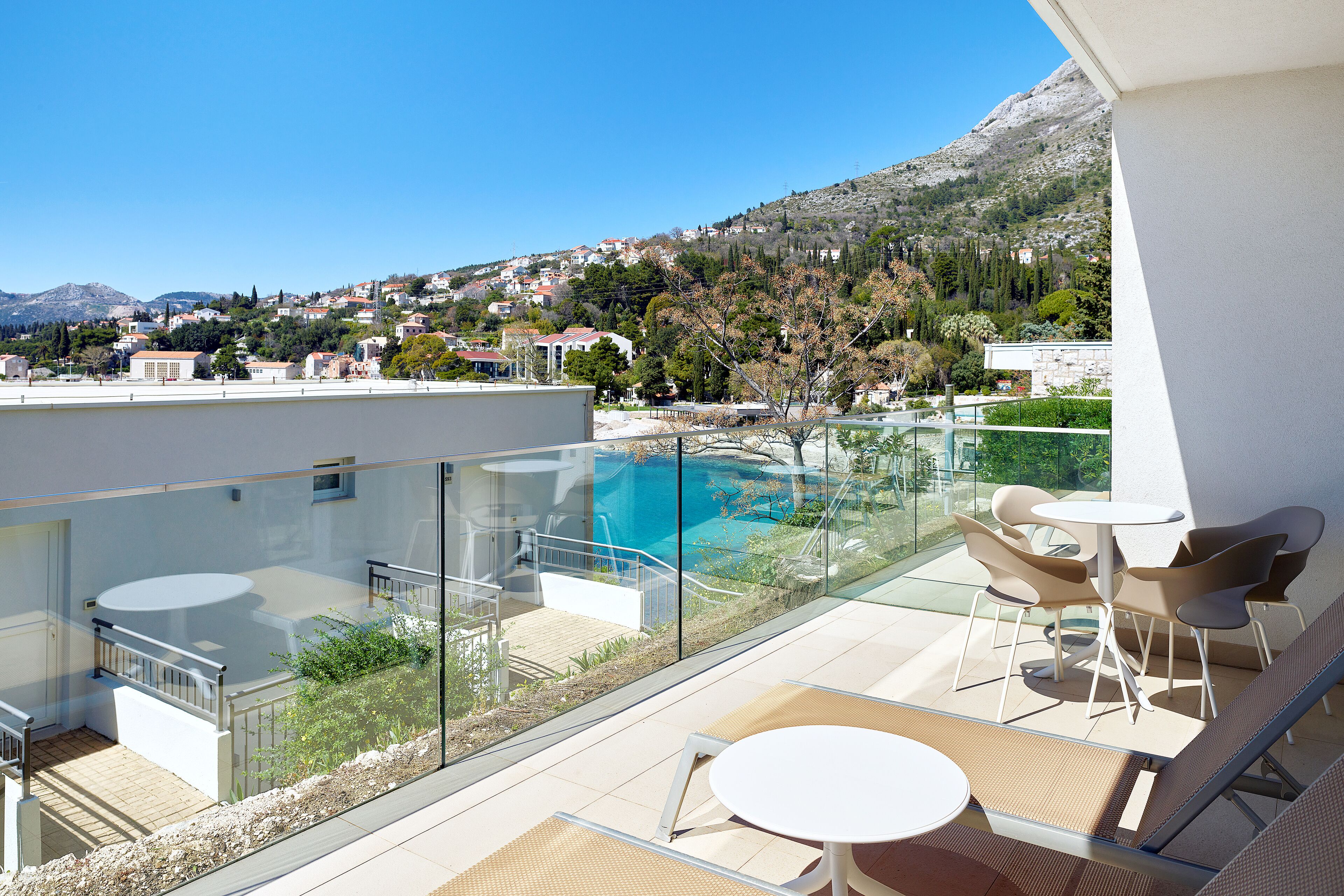 A balcony with a glass barrier overlooking a swimming pool and a mountainous landscape.