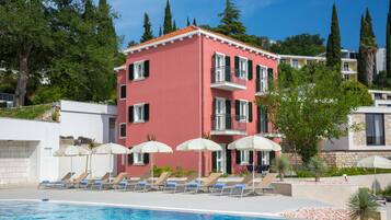 A hotel with a pool, sun loungers, and umbrellas.
