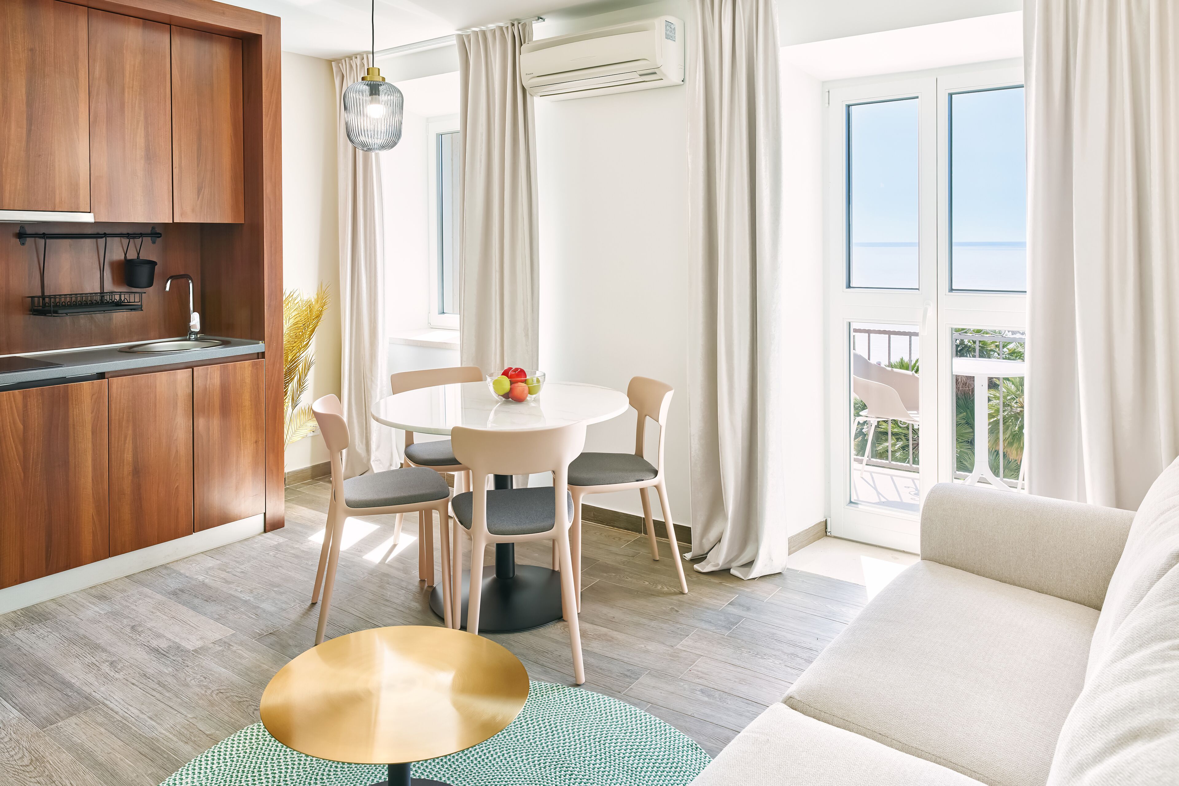 Una cocina moderna con armarios de madera, una mesa redonda con sillas, un sofá y un balcón con vistas.