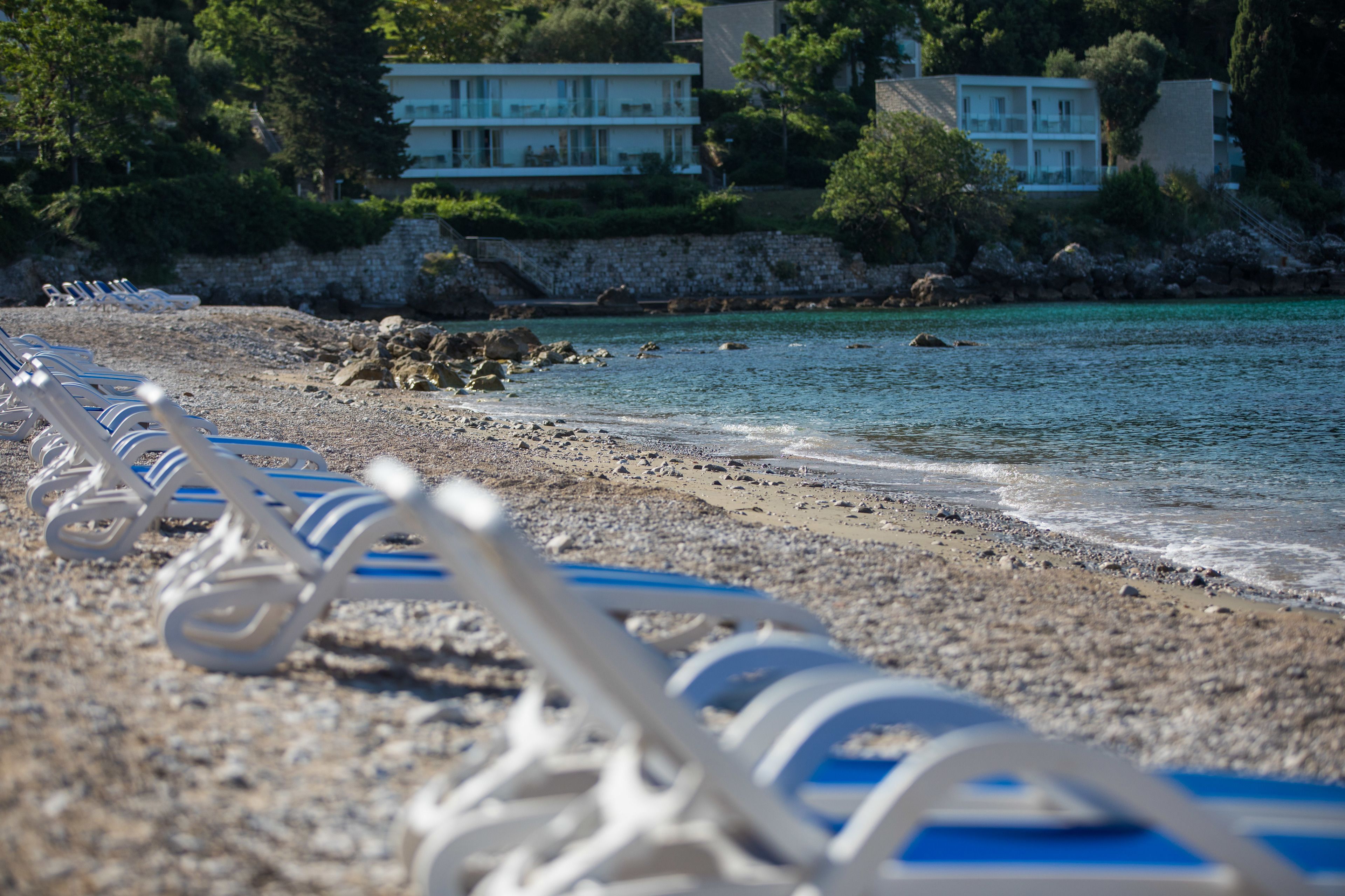 A beach with rows of white lounge chairs and a rocky shoreline.