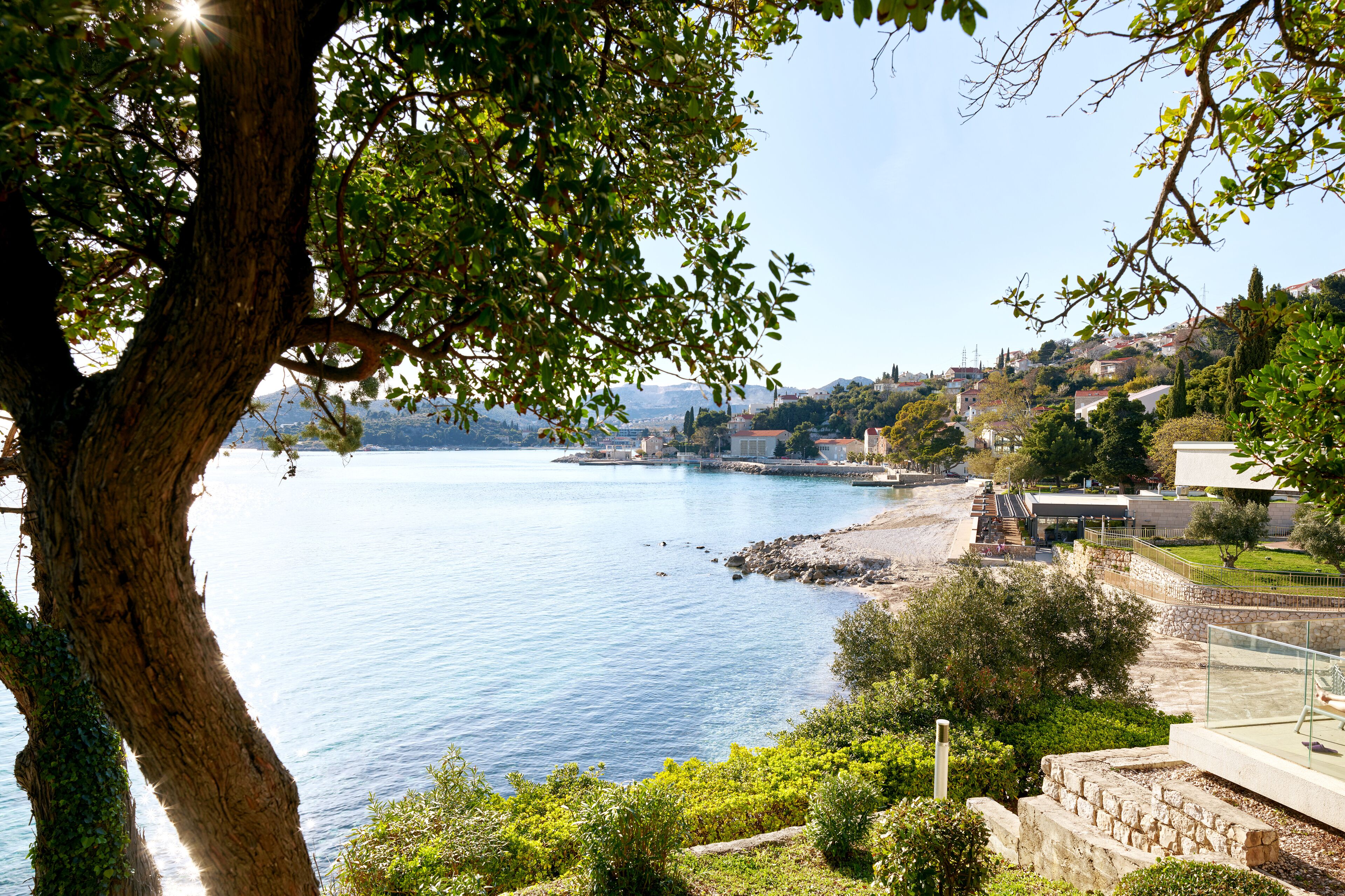 A coastal view with a clear sky, a body of water, and a hillside with buildings.