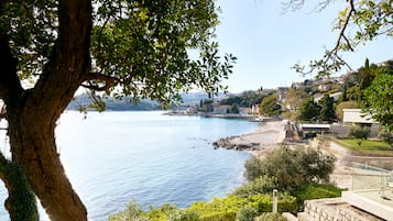 A coastal view with a clear sky, a body of water, and a hillside with buildings.