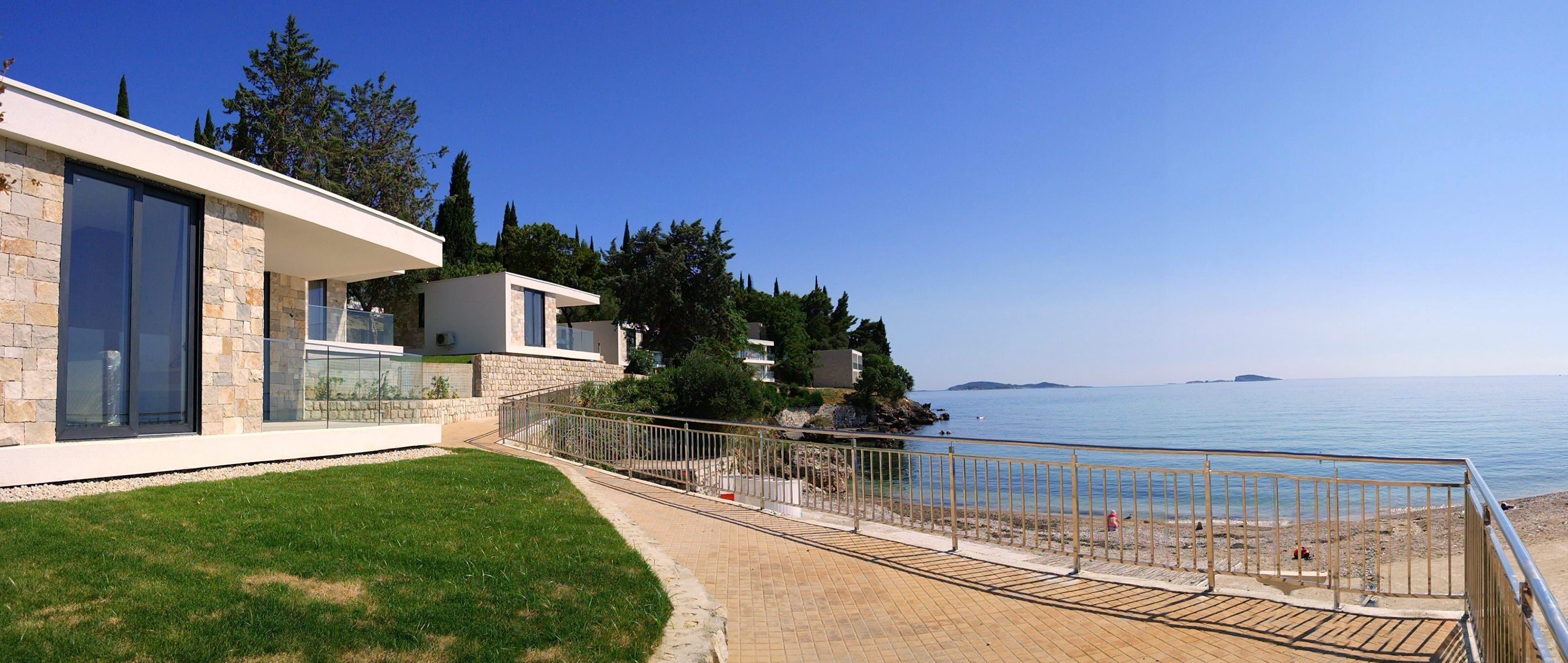 A modern coastal property with a stone facade, large windows, and a paved deck overlooking the sea.