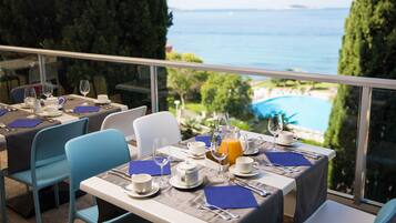 A dining area with tables set for breakfast, overlooking a pool and the sea.
