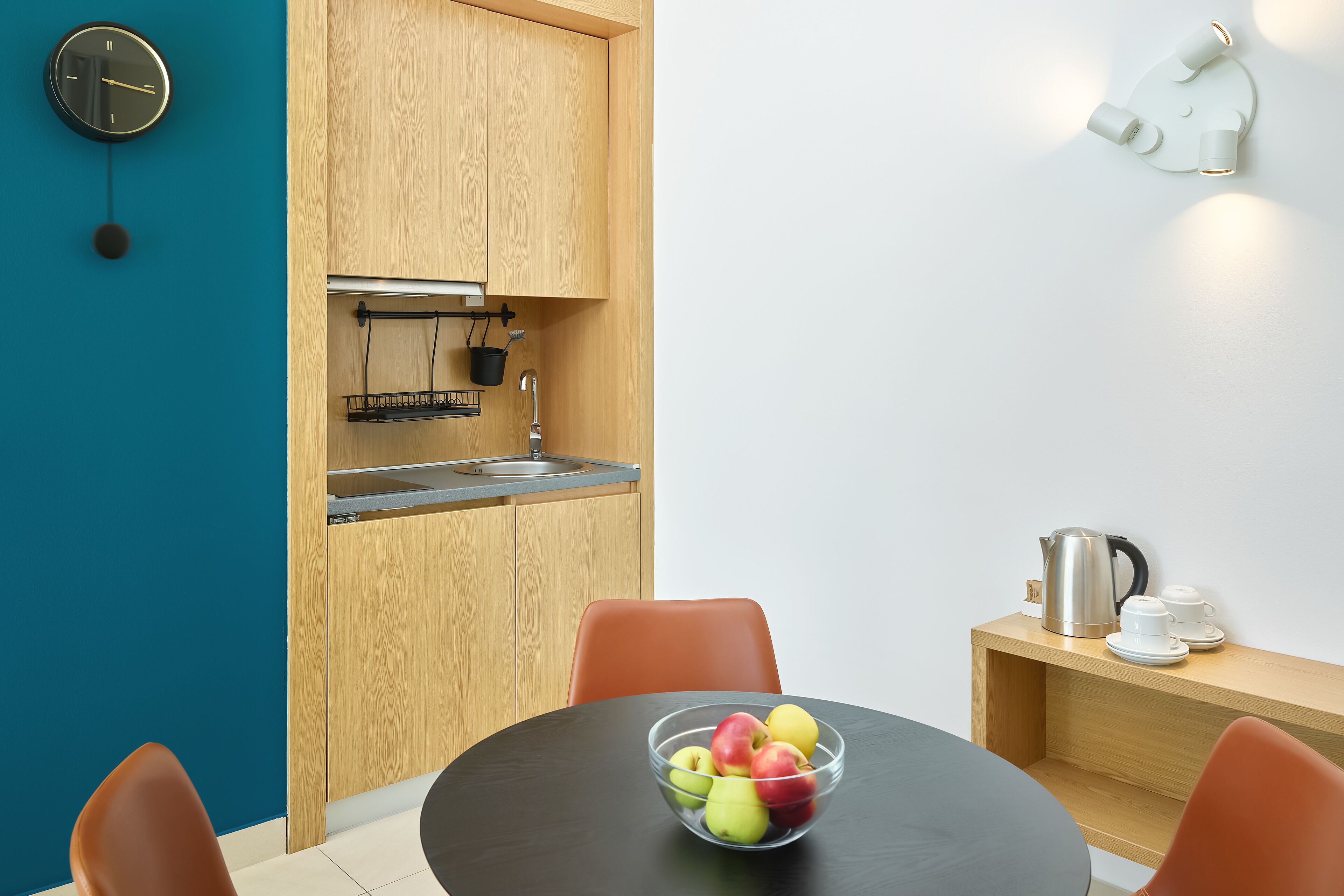 Een kleine keuken met een spoelbak, een waterkoker en een schaal fruit op tafel.