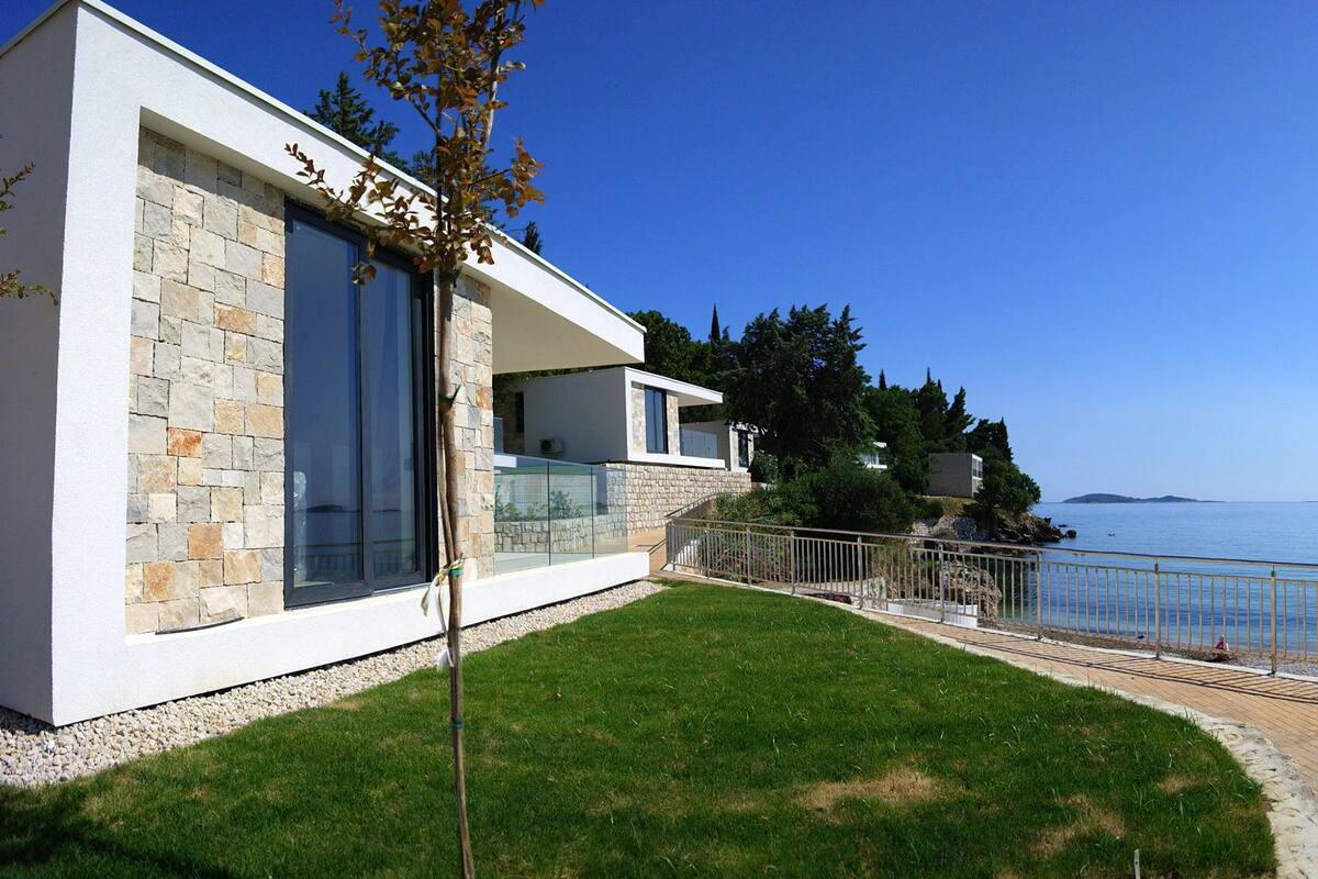 Une maison moderne avec une façade en pierre, de grandes fenêtres et une vue sur la mer.