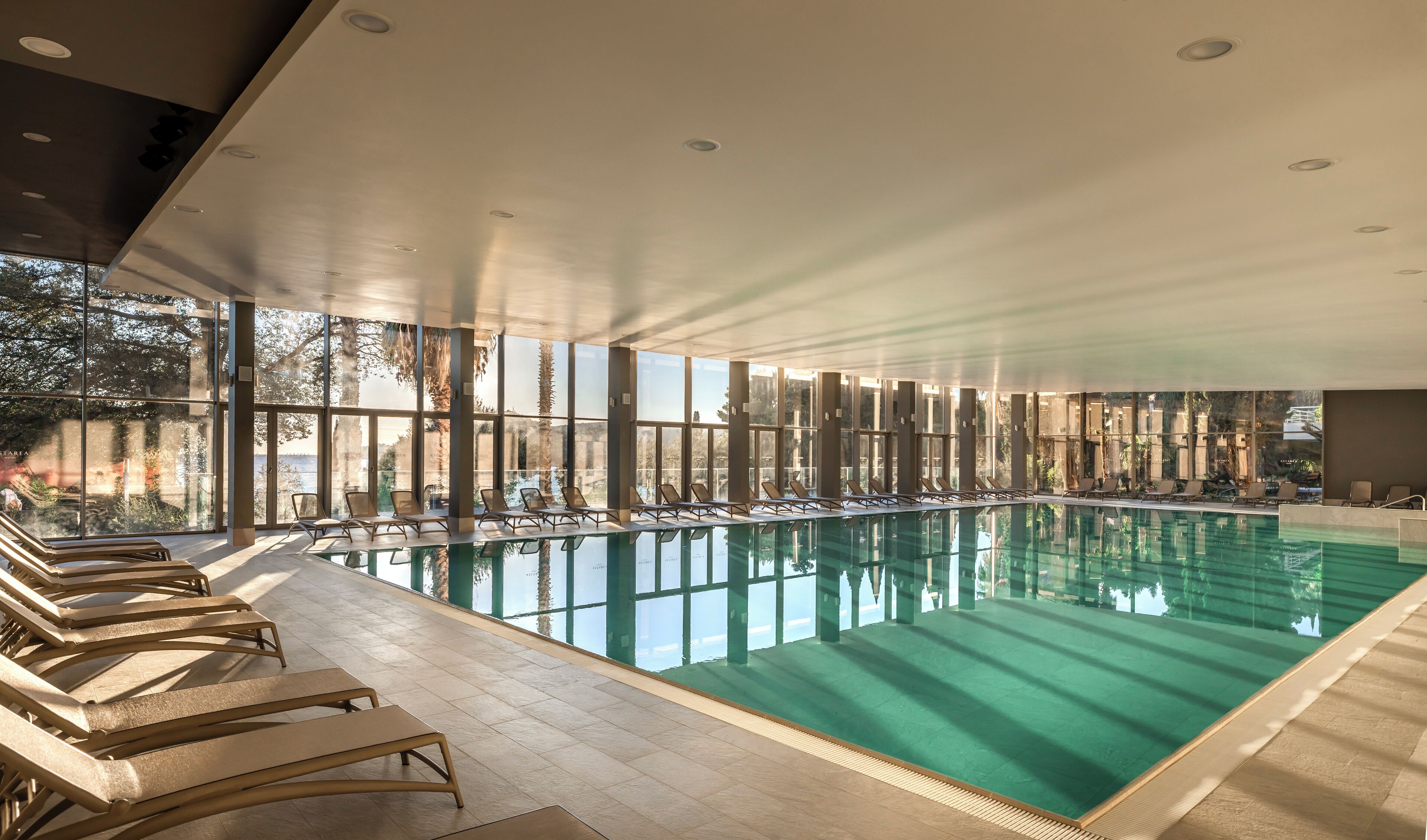 An indoor swimming pool with sunlit views and lounge chairs along the sides.