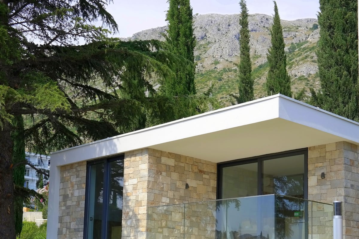 Une maison moderne avec une façade en pierre, de grandes fenêtres en verre et un toit plat.