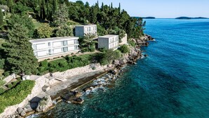 A coastal property with multiple modern buildings, a rocky shoreline, and clear blue sea.