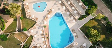 An aerial view of a resort with two swimming pools, sun loungers, and a landscaped garden.
