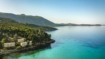 A coastal property with a clear view of the sea, lush greenery, and mountainous terrain in the background.