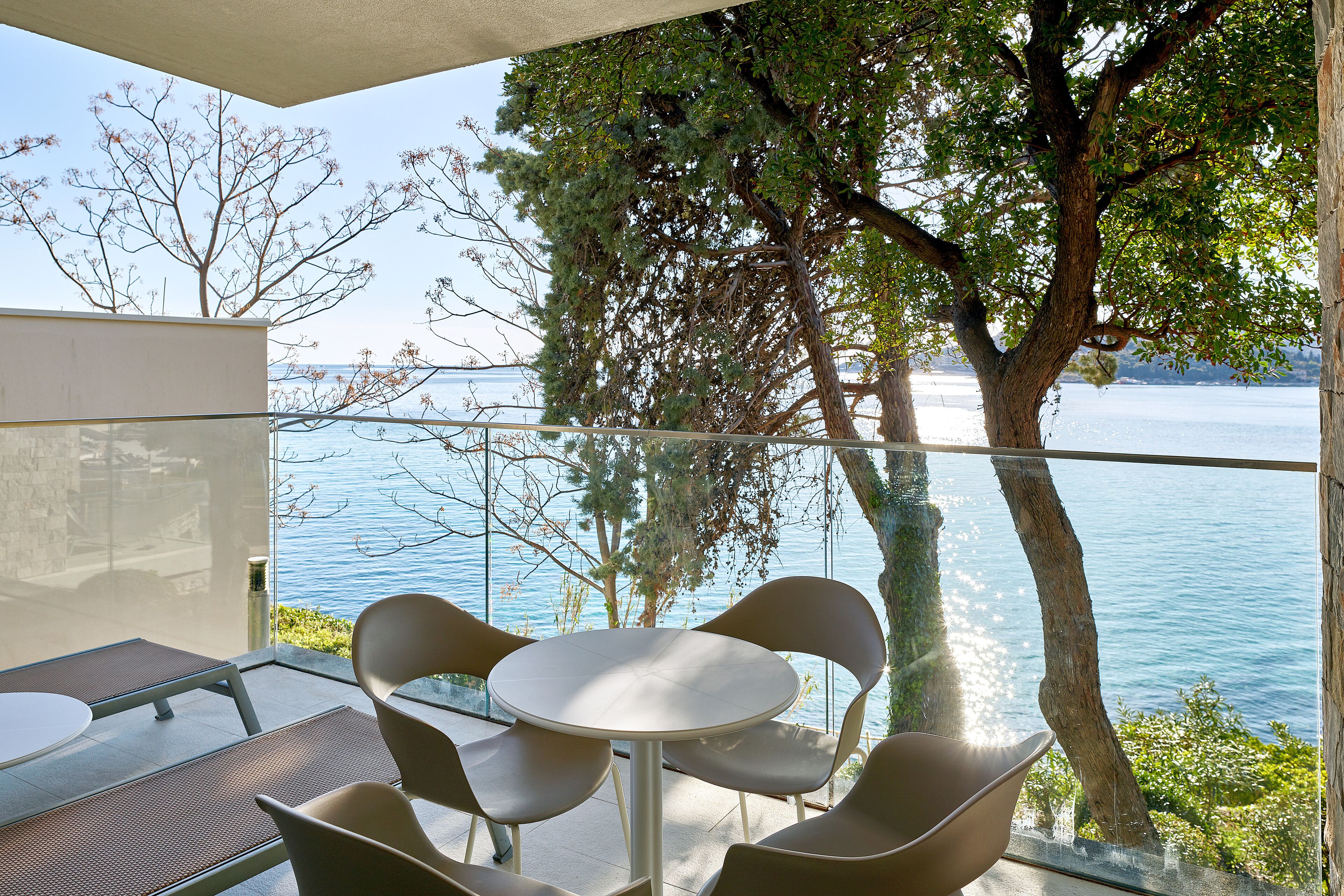 A modern outdoor seating area with a table and chairs, overlooking a body of water and surrounded by trees.