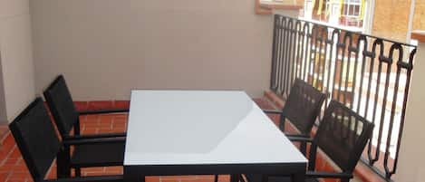 A terrace with a white table and four chairs, surrounded by a red-tiled floor and a metal railing.