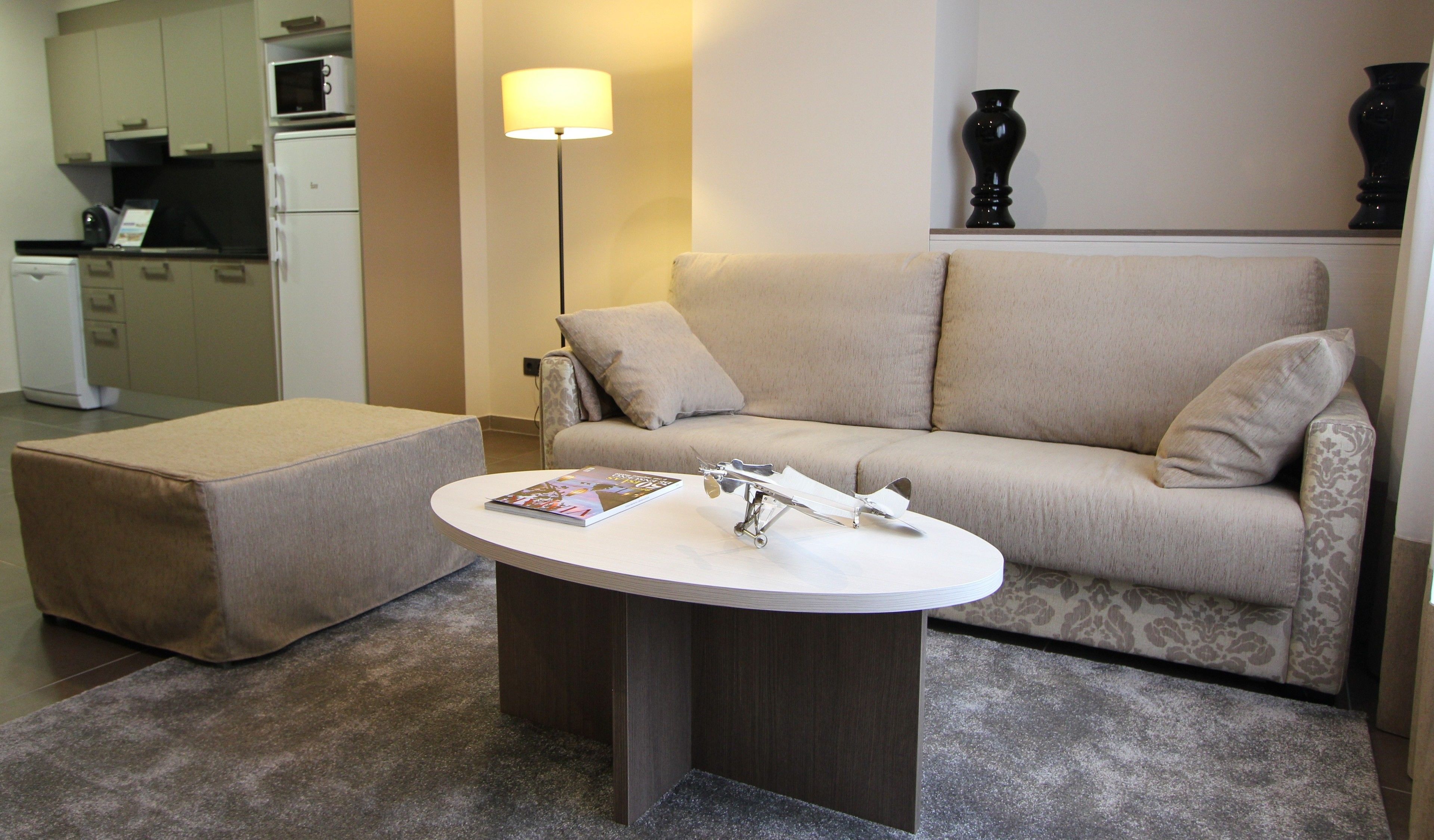 A living room with a sofa, ottoman, and a coffee table with a book and a model airplane.