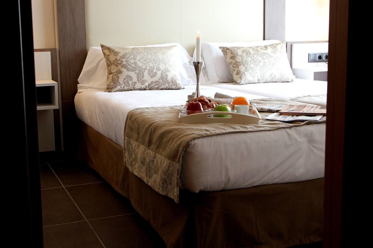 Une chambre d’hôtel avec un grand lit, deux oreillers, une table de chevet et une petite table de nuit.