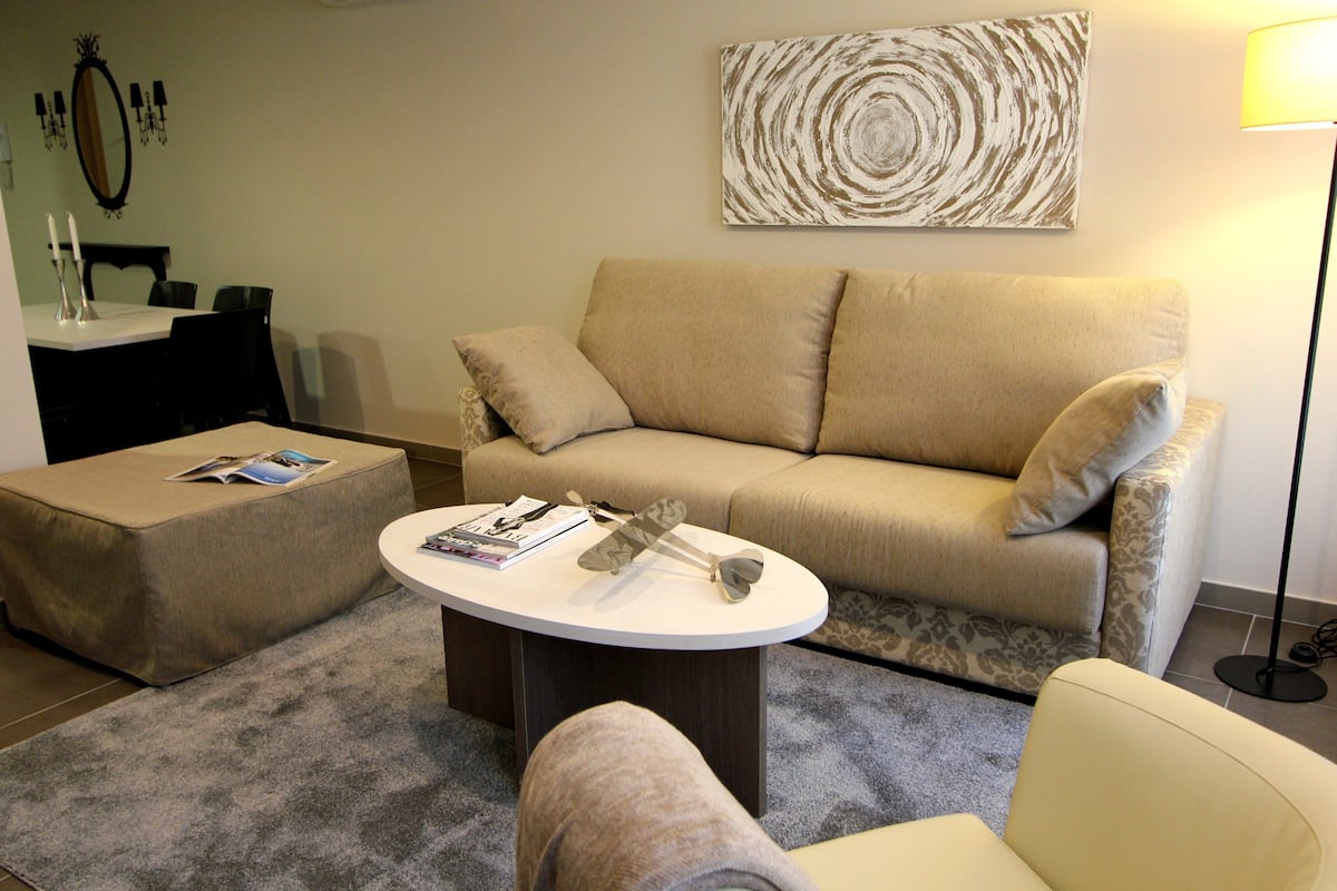 Un salon avec un canapé beige, une table basse ronde et un pouf assorti.