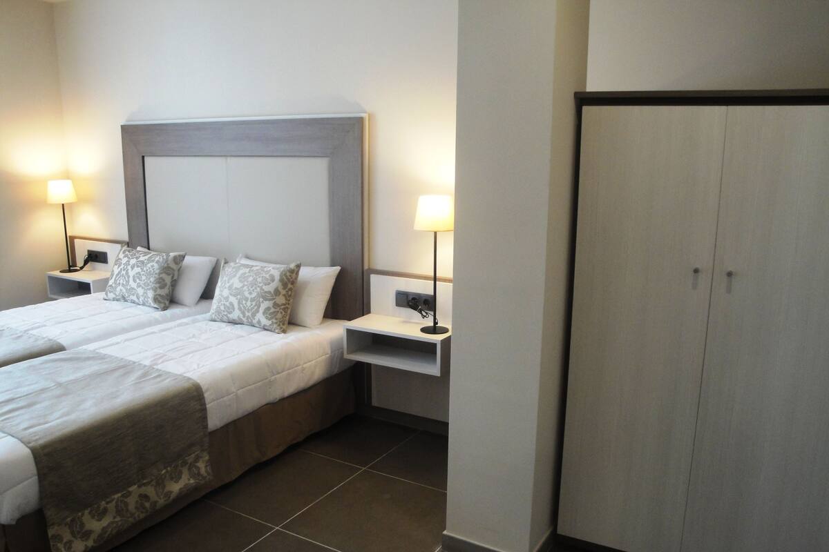 Une chambre d’hôtel avec deux lits, des tables de chevet avec des lampes, une armoire et un sol carrelé.