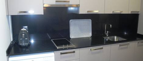 A modern kitchen with white cabinets, a black countertop, a built-in dishwasher, and a stainless steel sink.