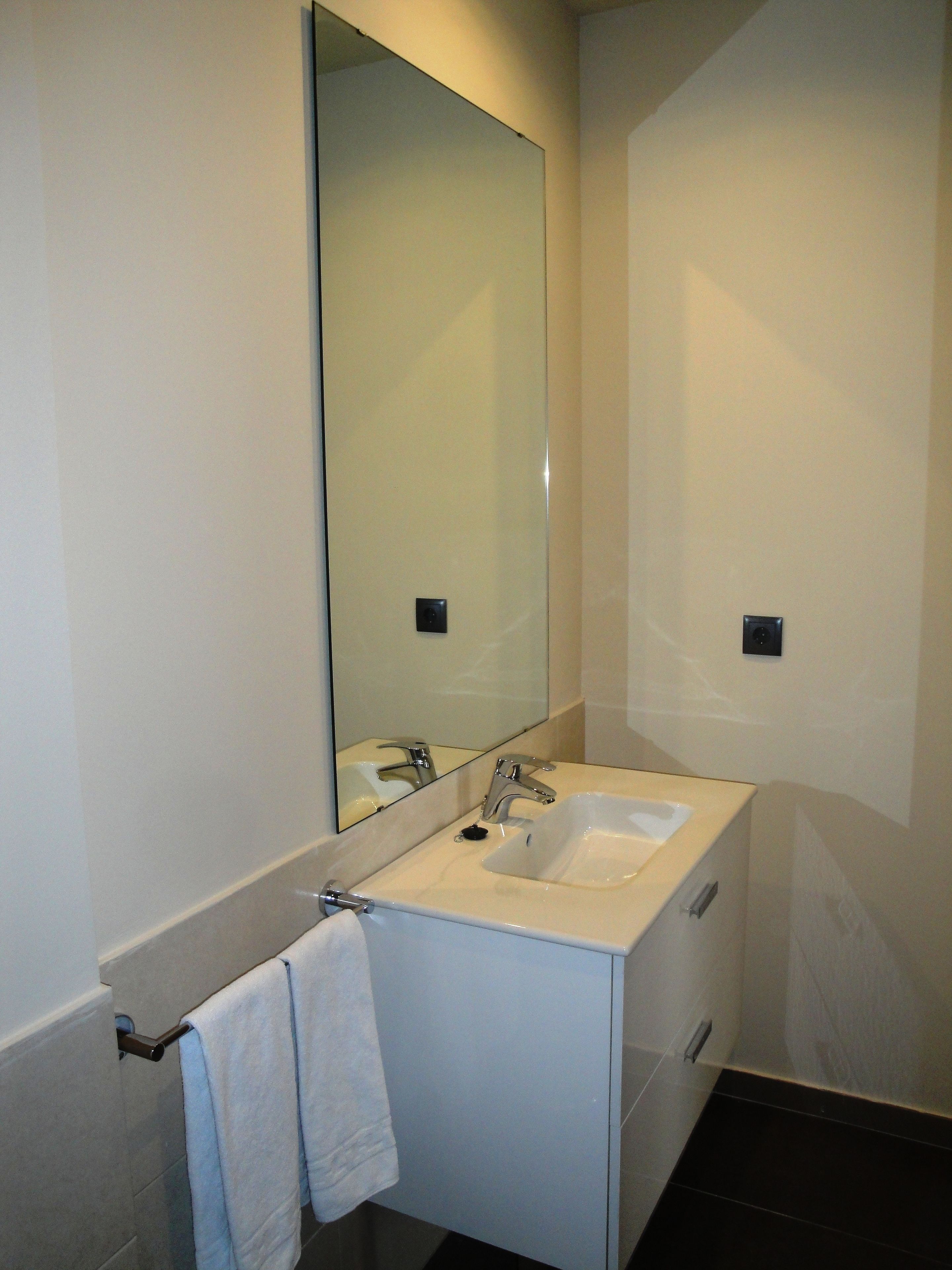 A modern bathroom with a large mirror, a white sink, and a towel rack.