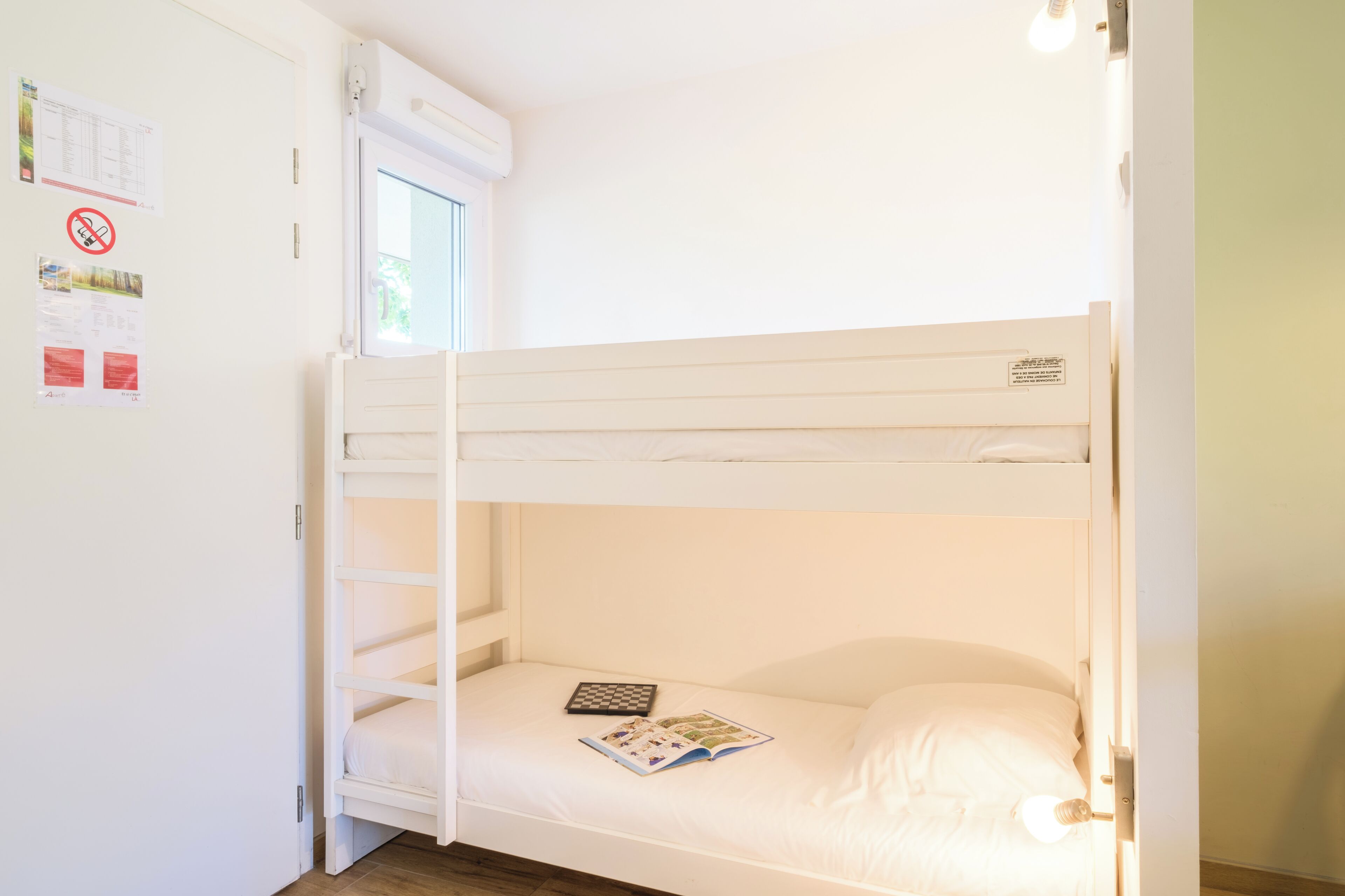 Un lit superposé avec une fenêtre, un climatiseur fixé au mur et un luminaire.