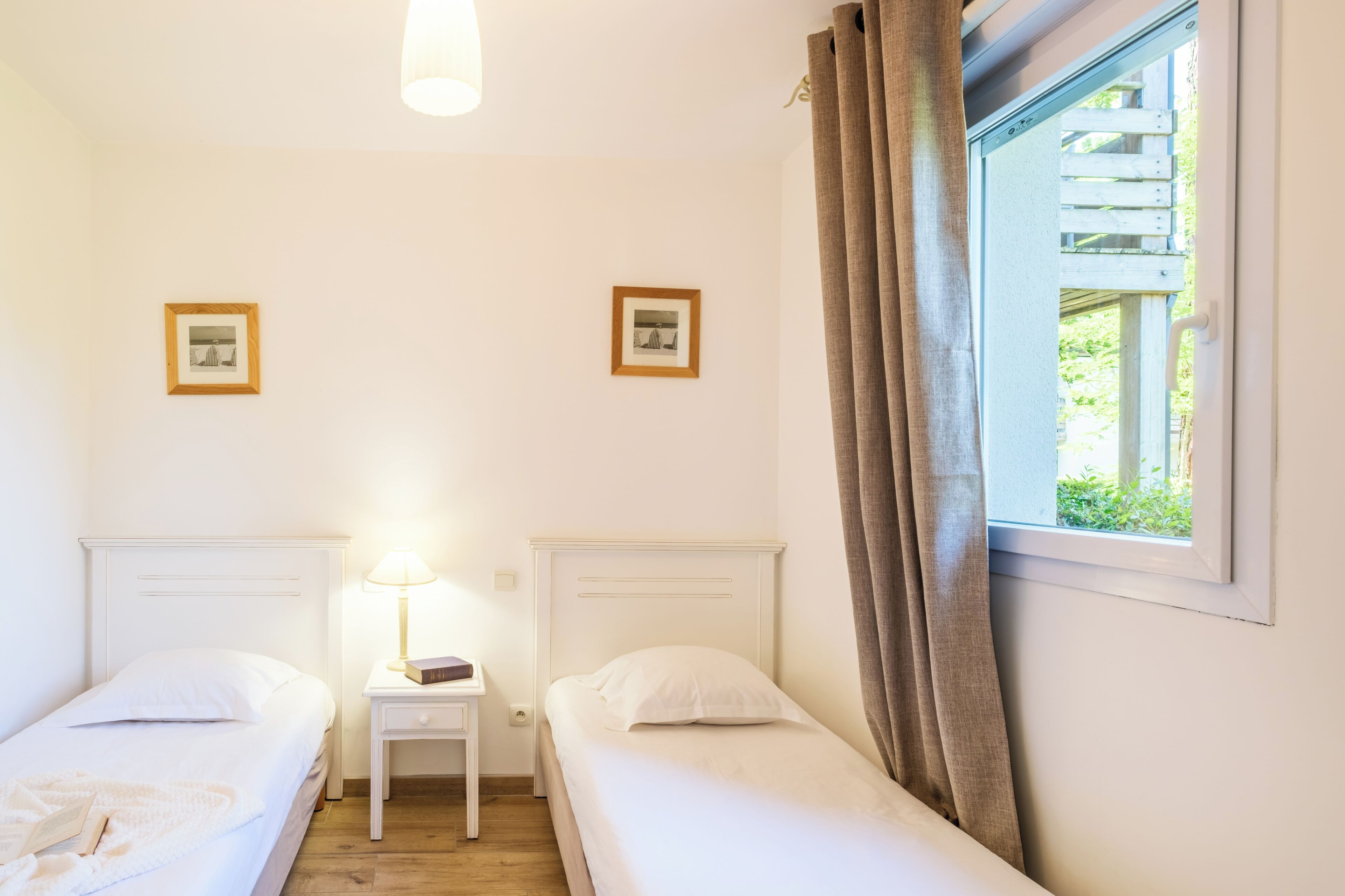 Un dormitorio con dos camas individuales, una mesita de noche con lámpara y dos cuadros en la pared.