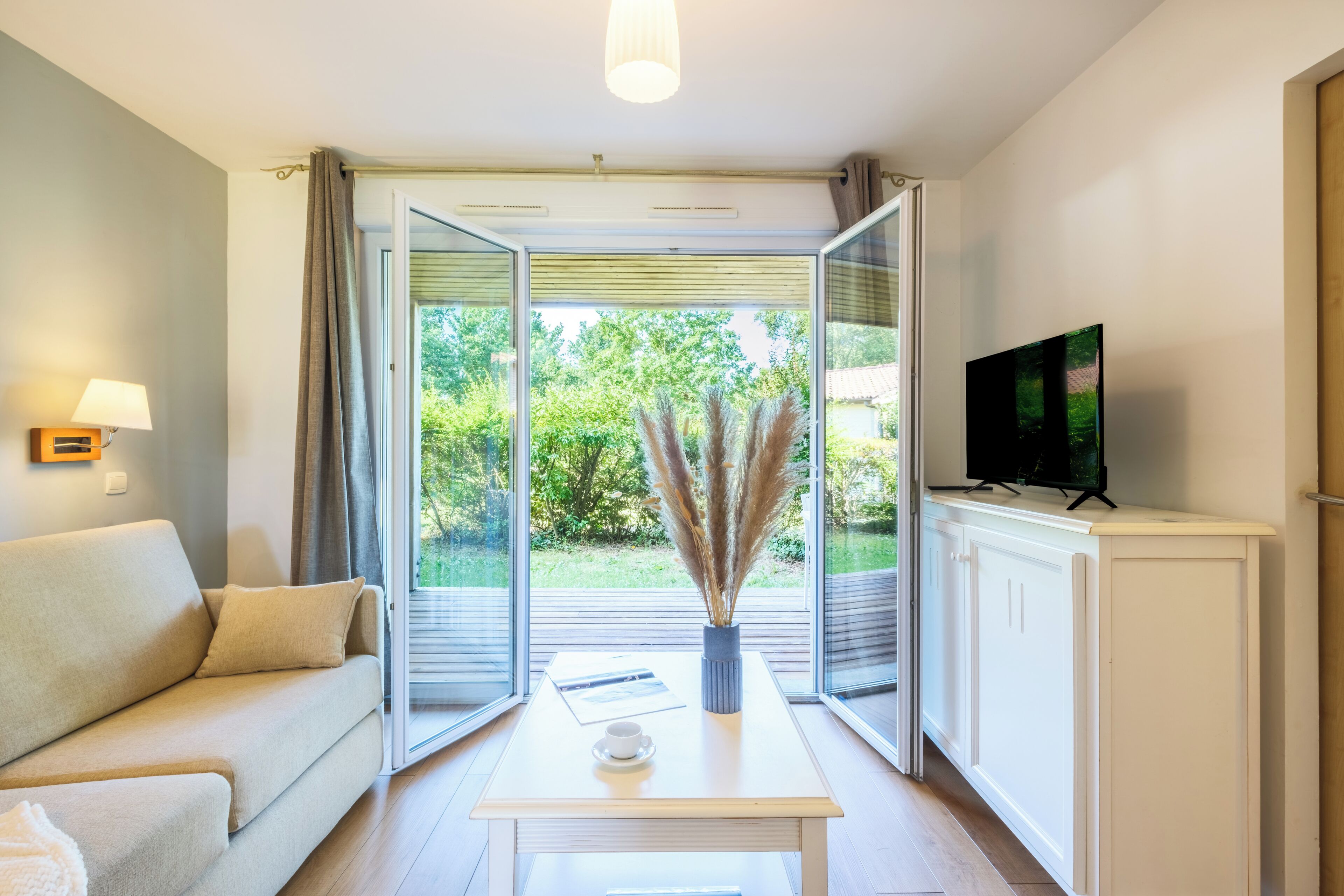 Un salon moderne comprenant un canapé, une table basse, un téléviseur et une vue sur la verdure grâce à de grandes portes vitrées.