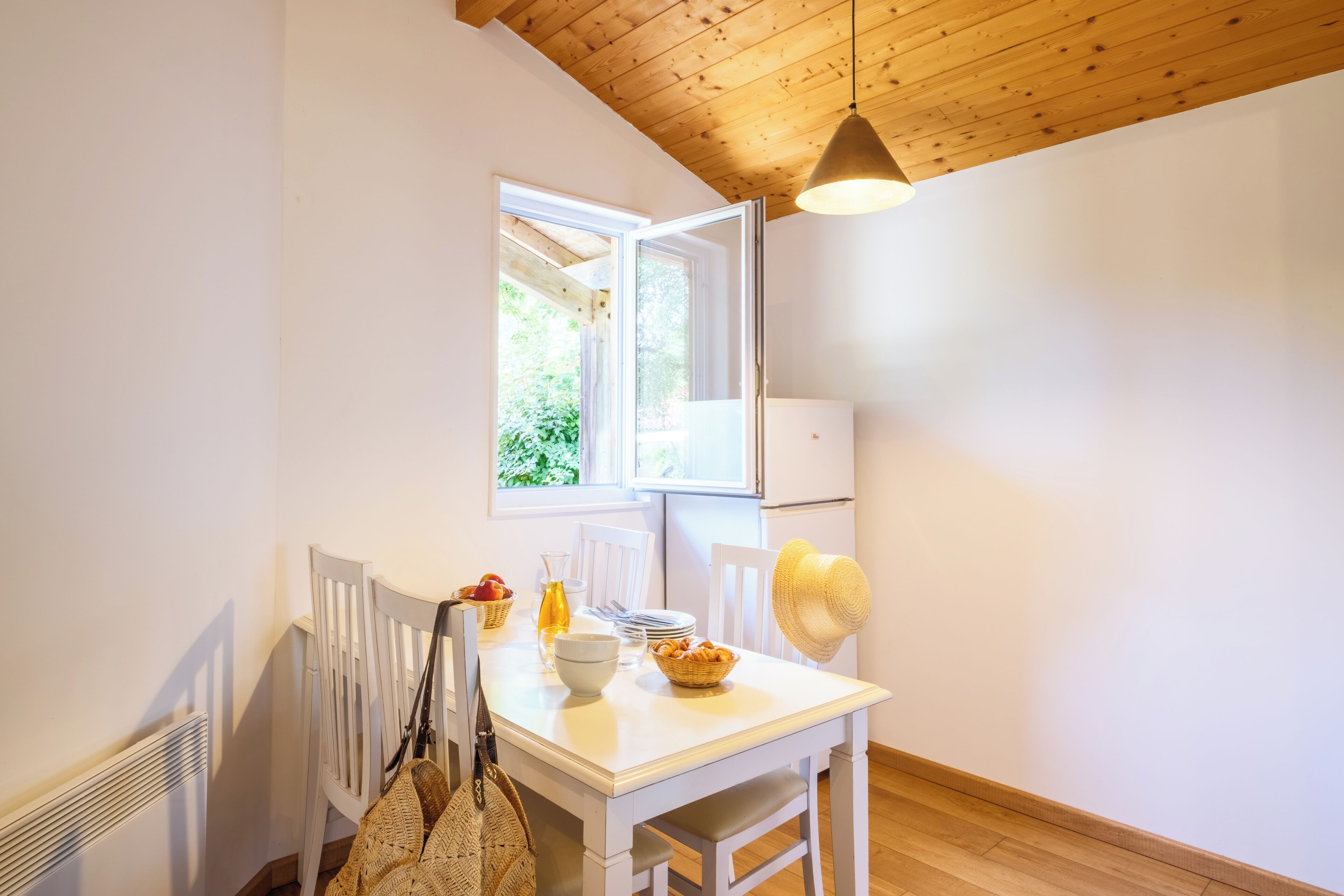 Une pièce avec une table blanche, une fenêtre, un radiateur et un luminaire suspendu.