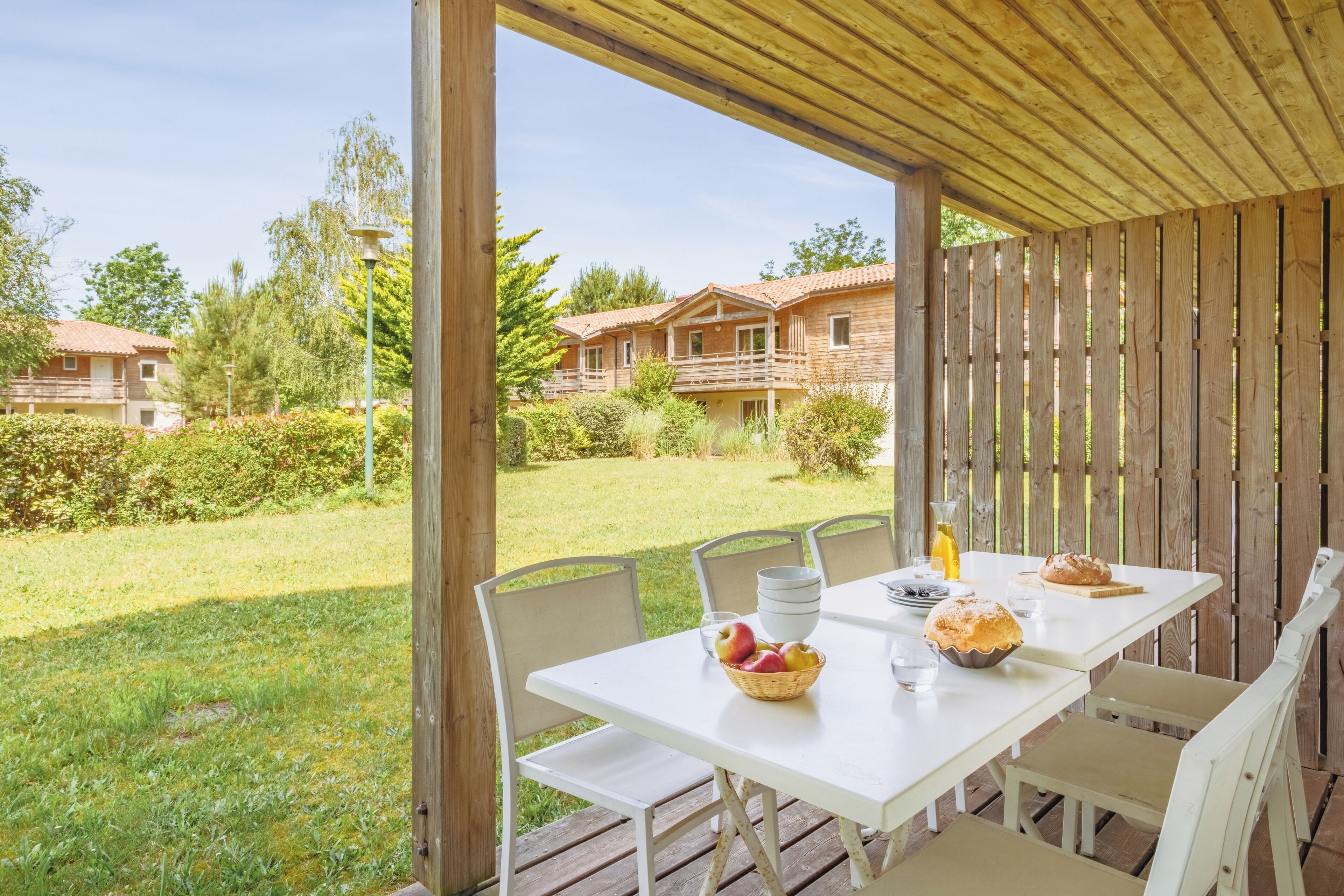 A covered outdoor dining area with a table set for two, surrounded by chairs.