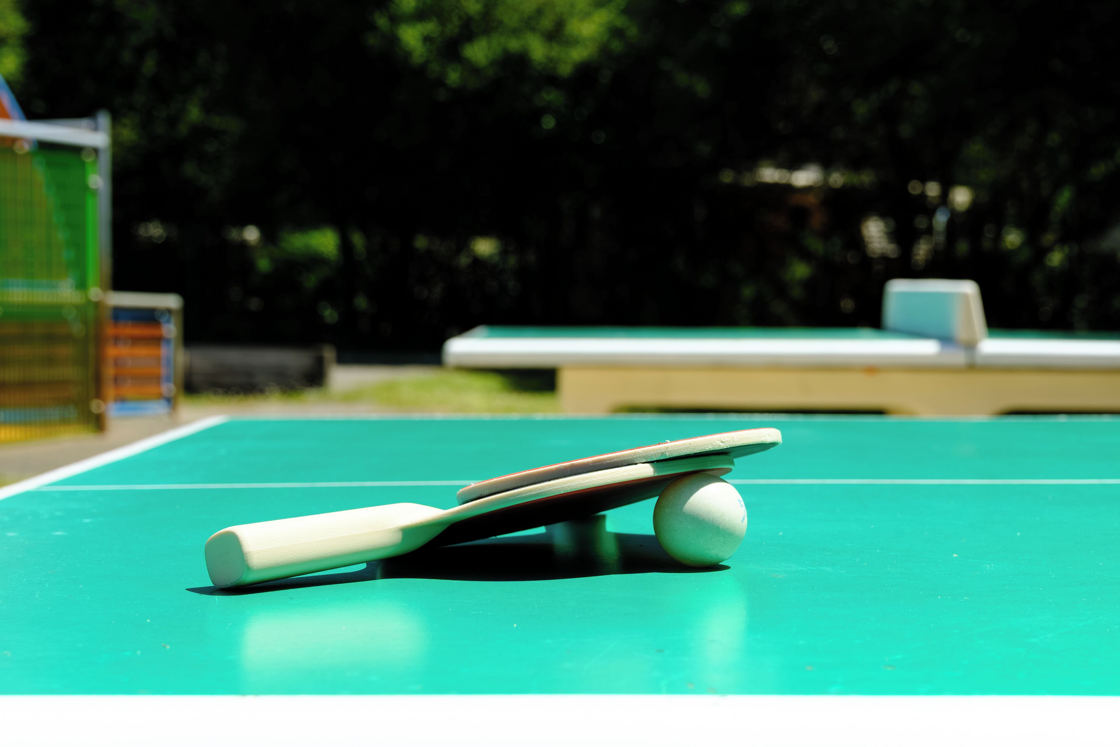 Ett bordtennisbord med ett racket och en boll, och ett biljardbord i bakgrunden.