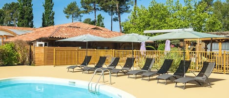 Una piscina con sillas de descanso y sombrillas, rodeada de vallas de madera y árboles.