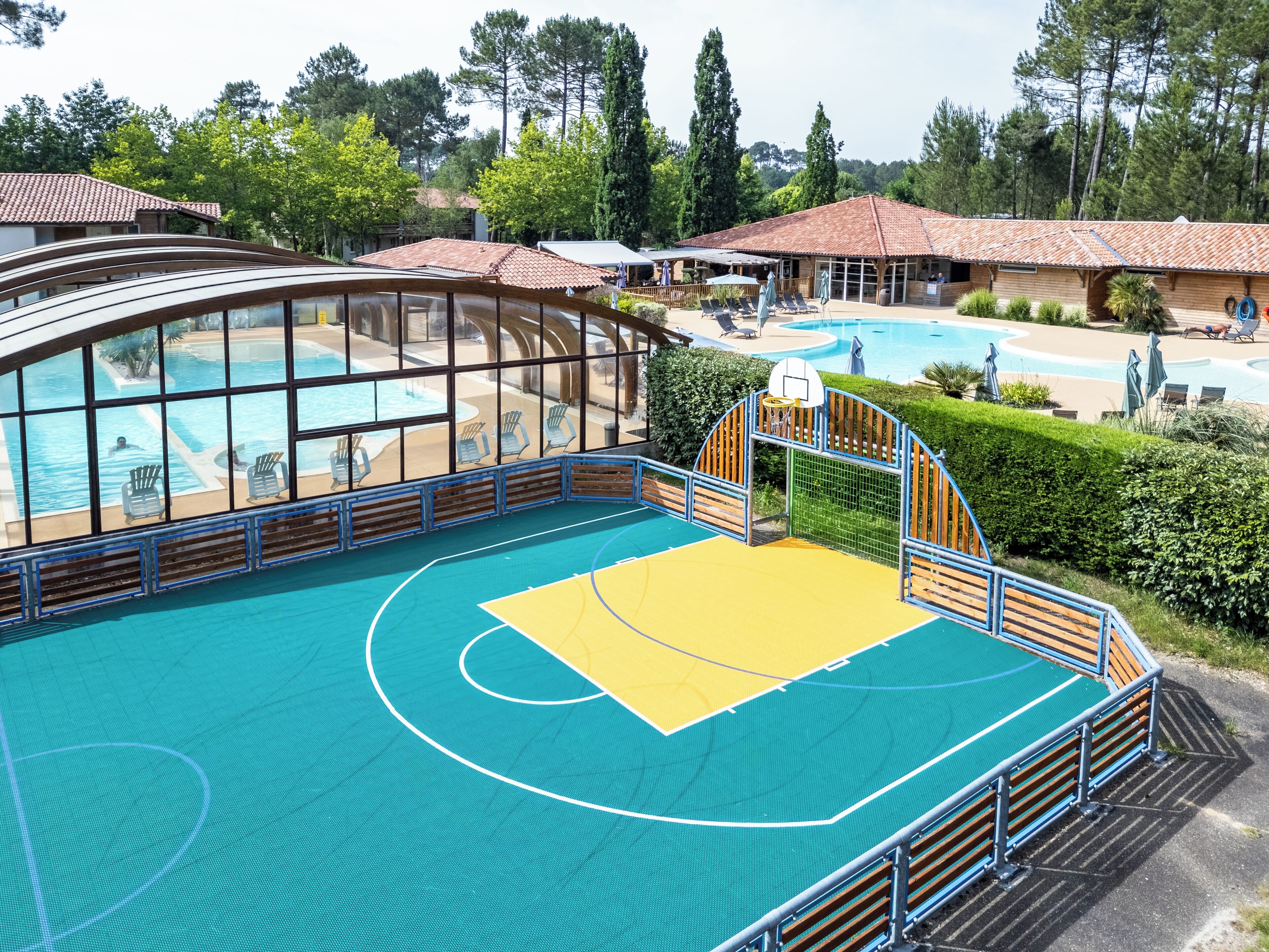 A pool area with a basketball court, lounge chairs, and a covered seating area.
