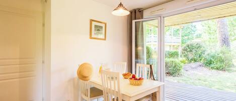 Un espace repas comprenant une table, des chaises, un luminaire suspendu, un tableau encadré au mur et une vue sur l’extérieur grâce à une porte coulissante.