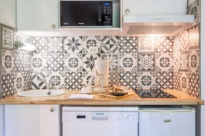 A kitchen with patterned tiles, a microwave, a coffee maker, a bread loaf, and a dishwasher. - Résidence Pierre & Vacances Les Cottages du Lac (Parentis-en-Born)